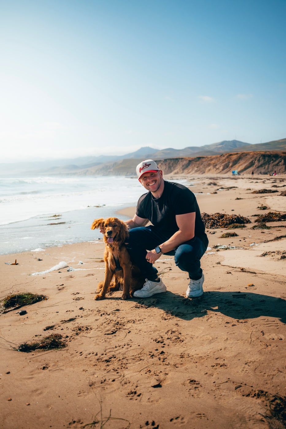 Max kneeling with his golden retriever on a California beach
