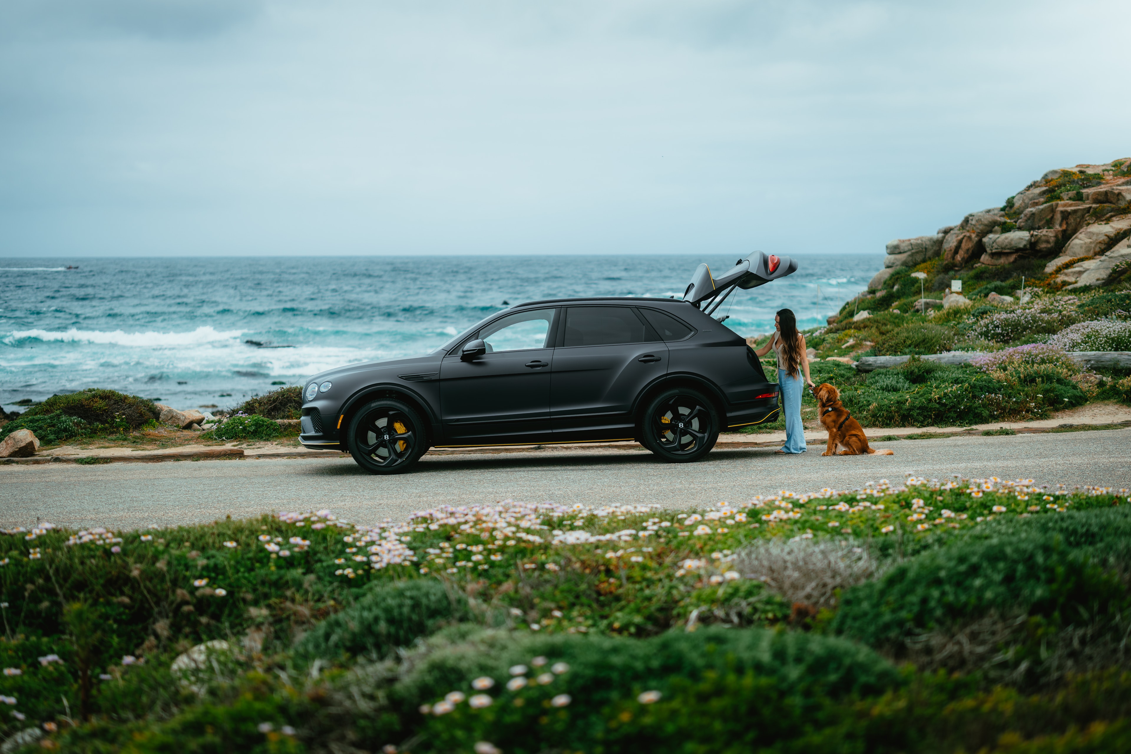 Bentayga with rear hatch open, woman and golden retriever at the Pacific