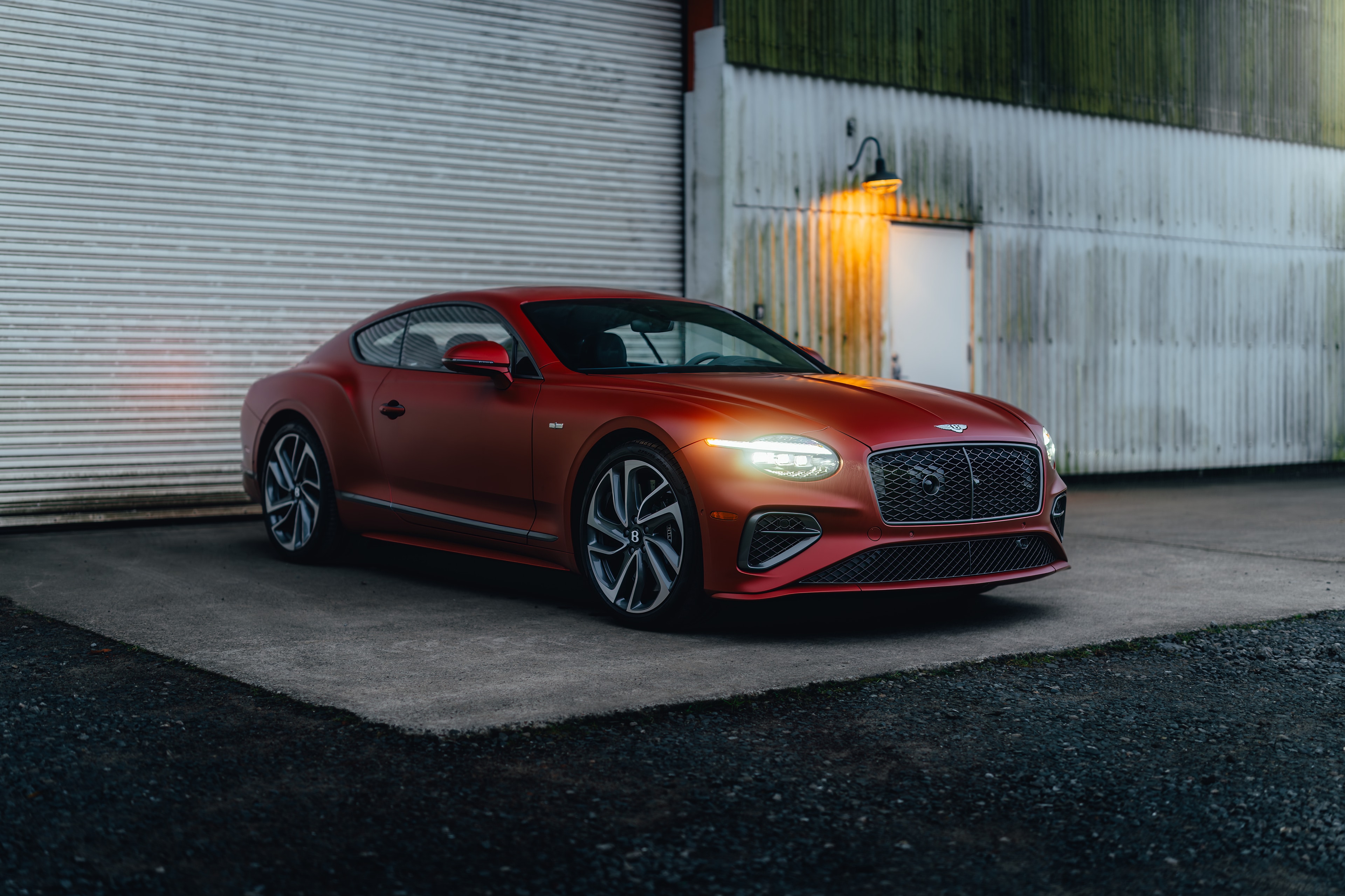 Continental GT front three-quarter at an industrial corrugated wall, warm yard light