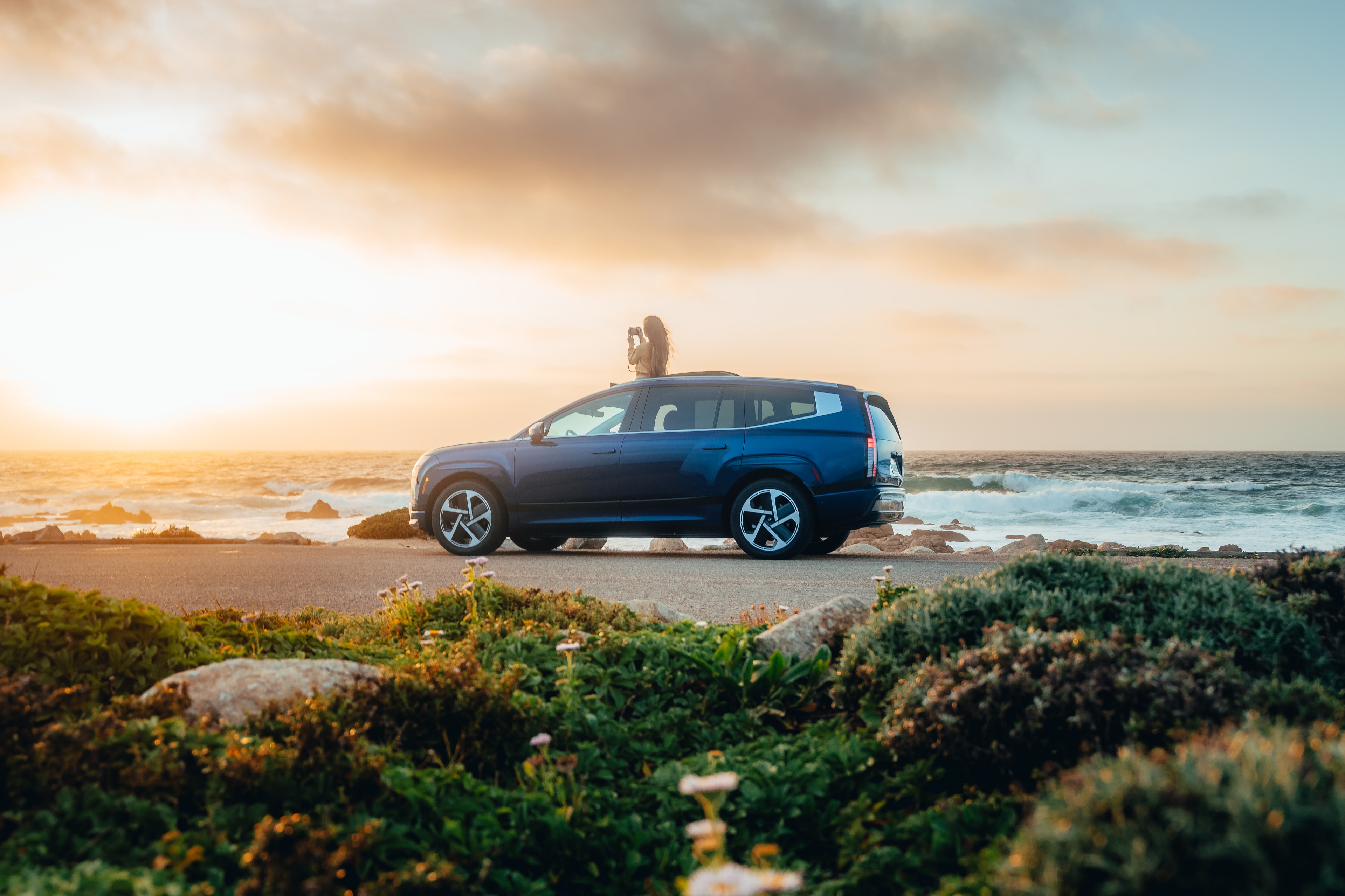 Hyundai IONIQ 9 side profile at sunset on the Big Sur coast, a passenger up through the roof