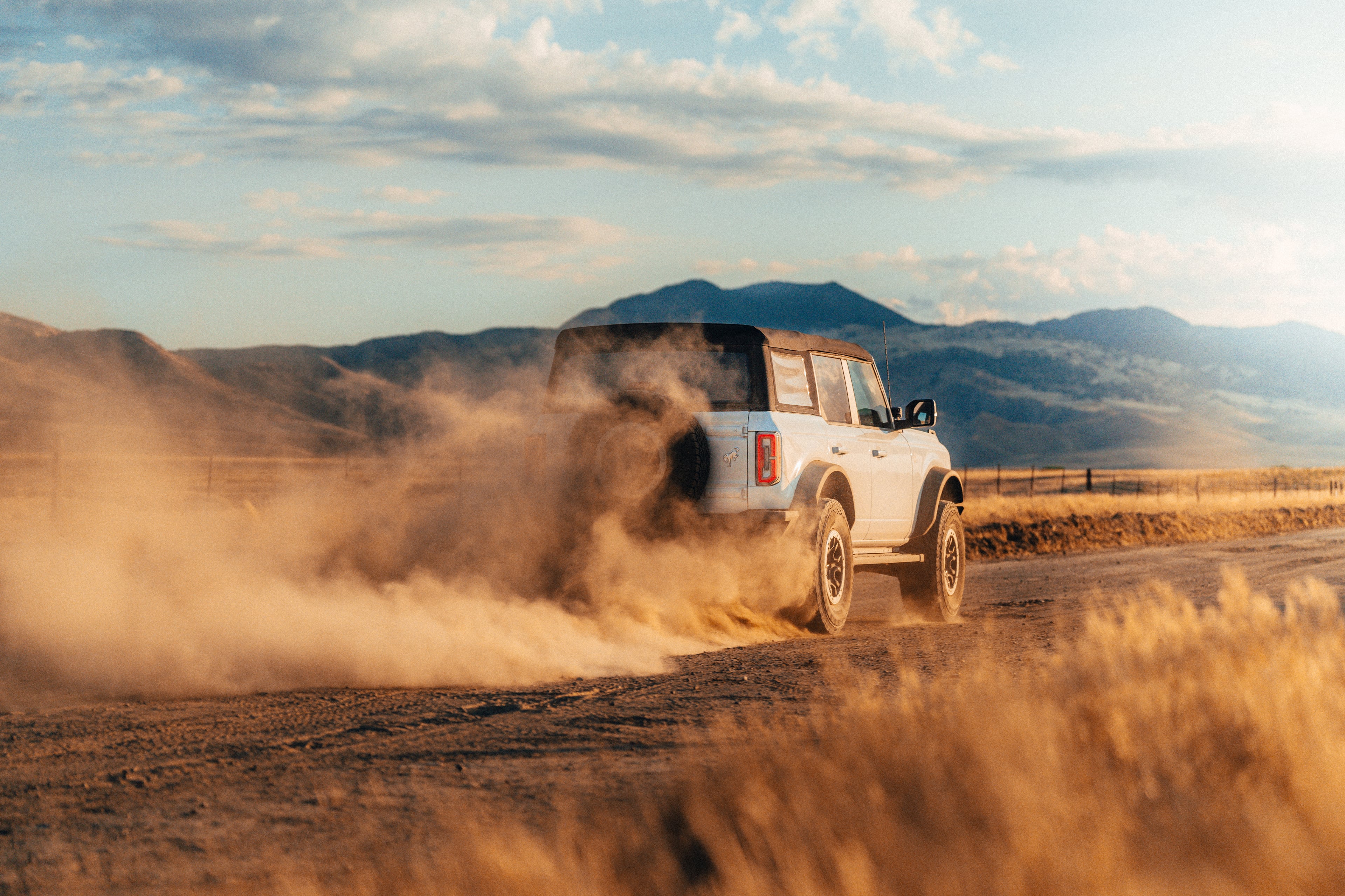 Ford Bronco kicking up dust on a golden-hour backroad with mountain backdrop