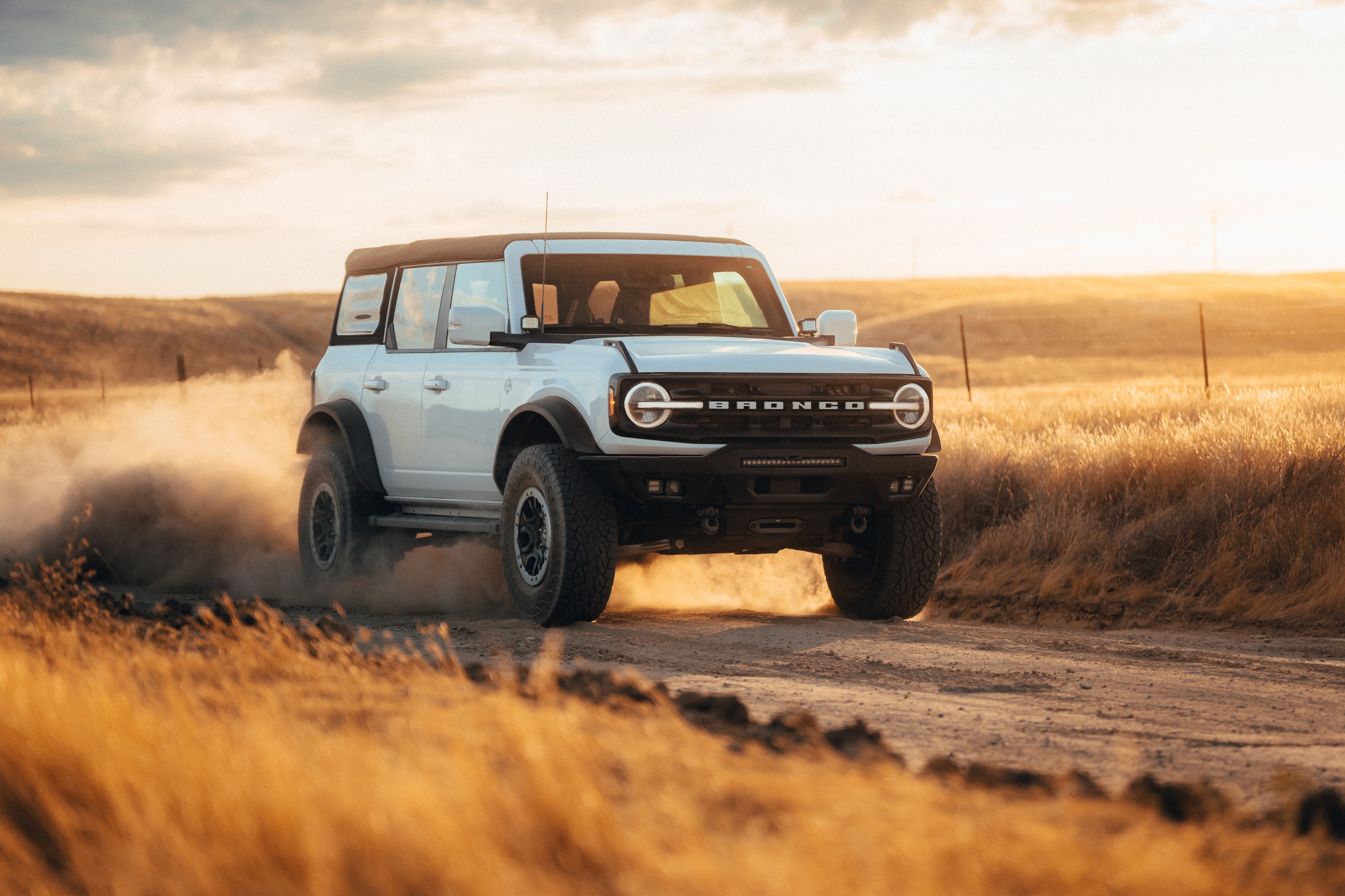 Ford Bronco kicking up dust on a golden-hour backroad through the California hills