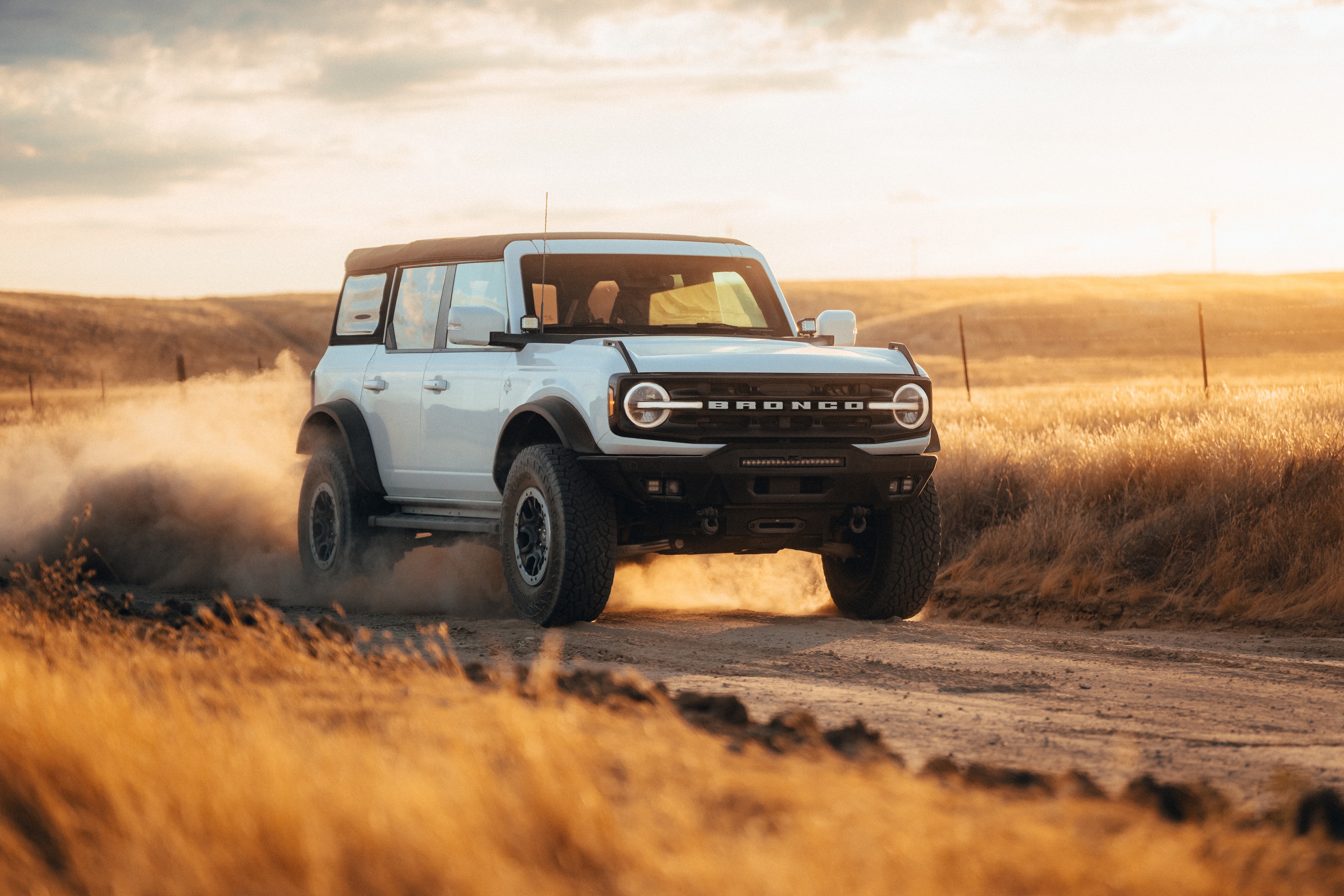 Ford Bronco kicking dust on a golden-hour backroad, California hills