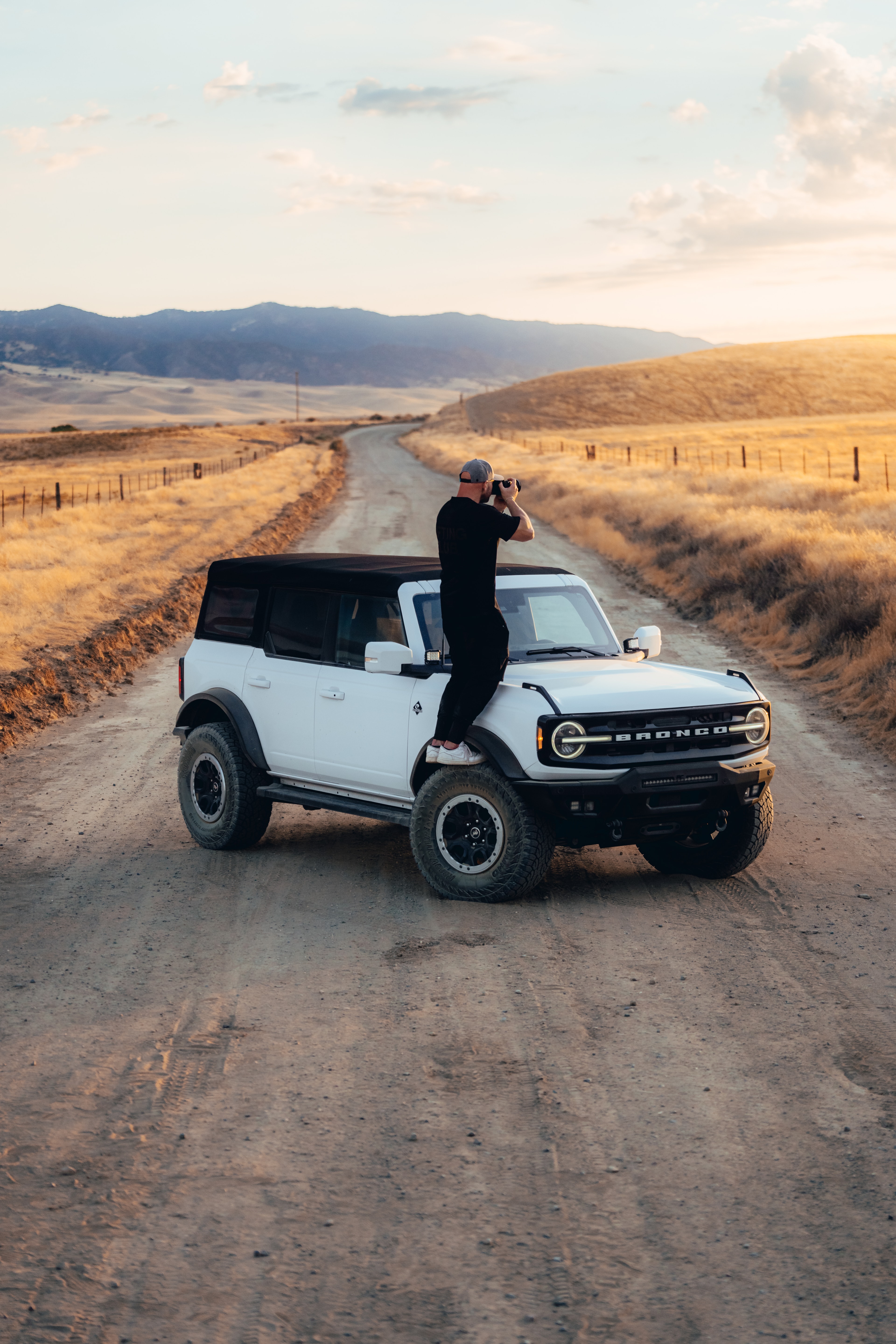 Max Loew on the hood of the Ford Bronco shooting back at the camera, golden-hour California ranch road