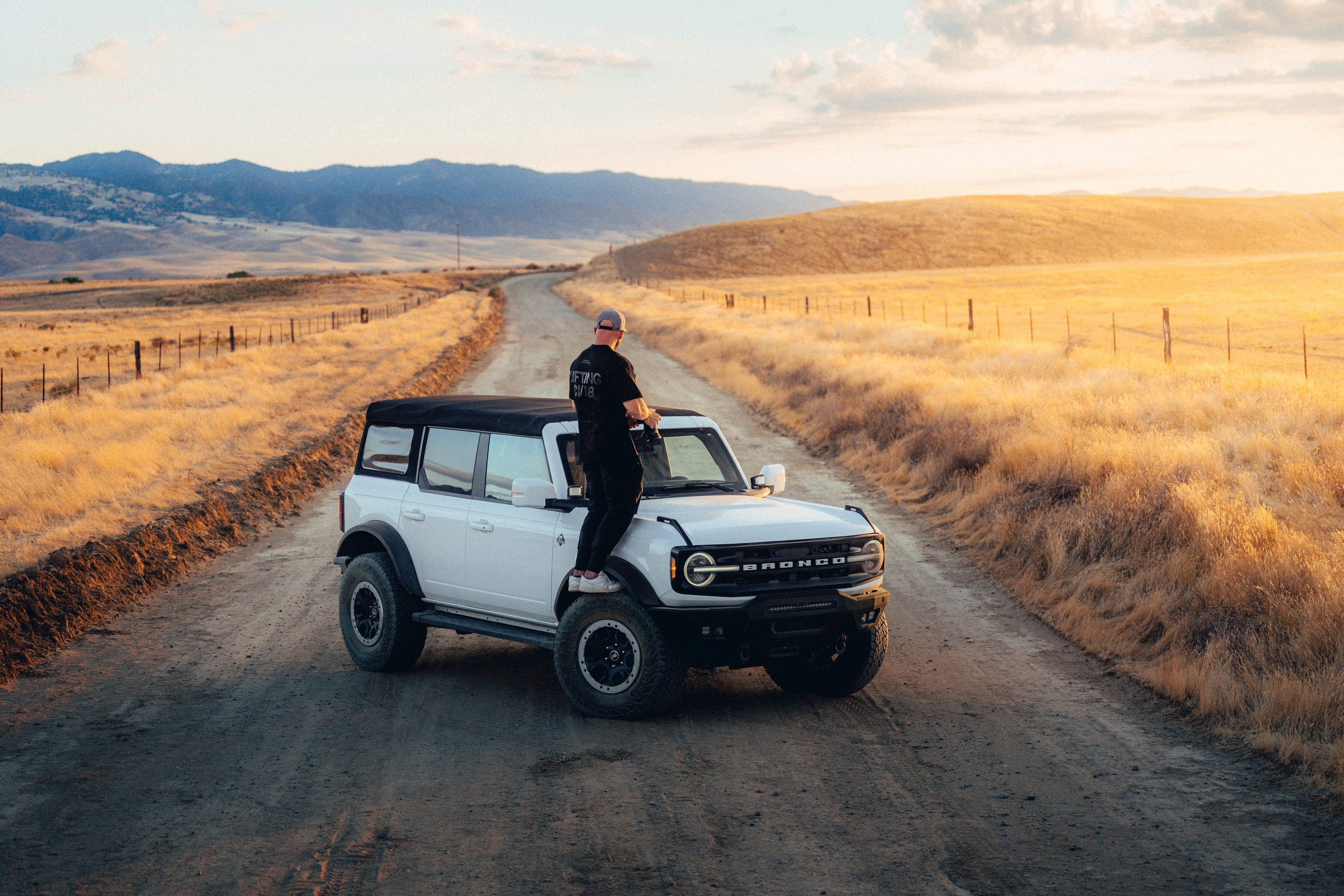 Max Loew on the hood of the Ford Bronco, dirt road stretching to the California mountains