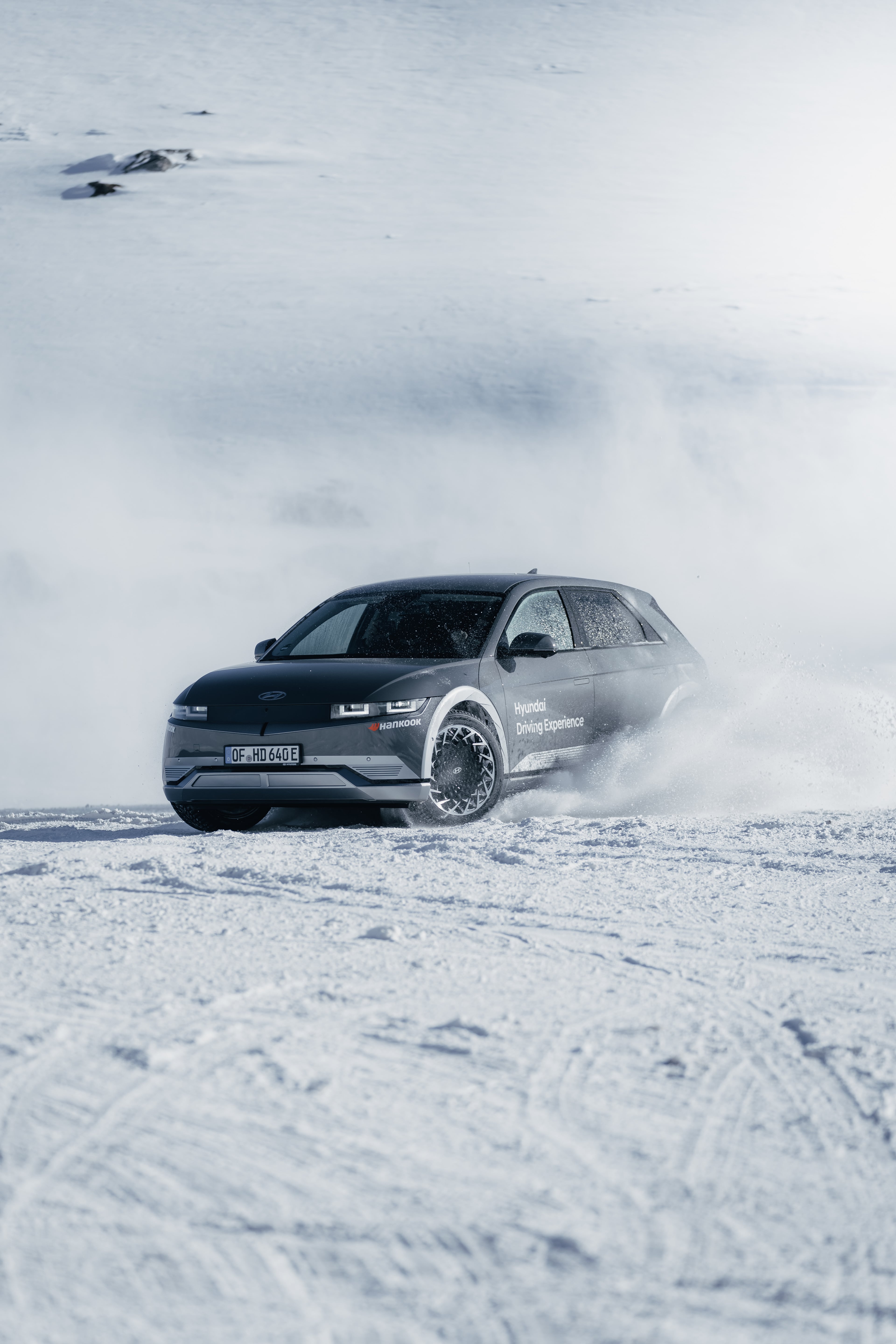 Hyundai IONIQ 5 mid-drift on the glacier, Hyundai Driving Experience livery, snow spray off studded tires