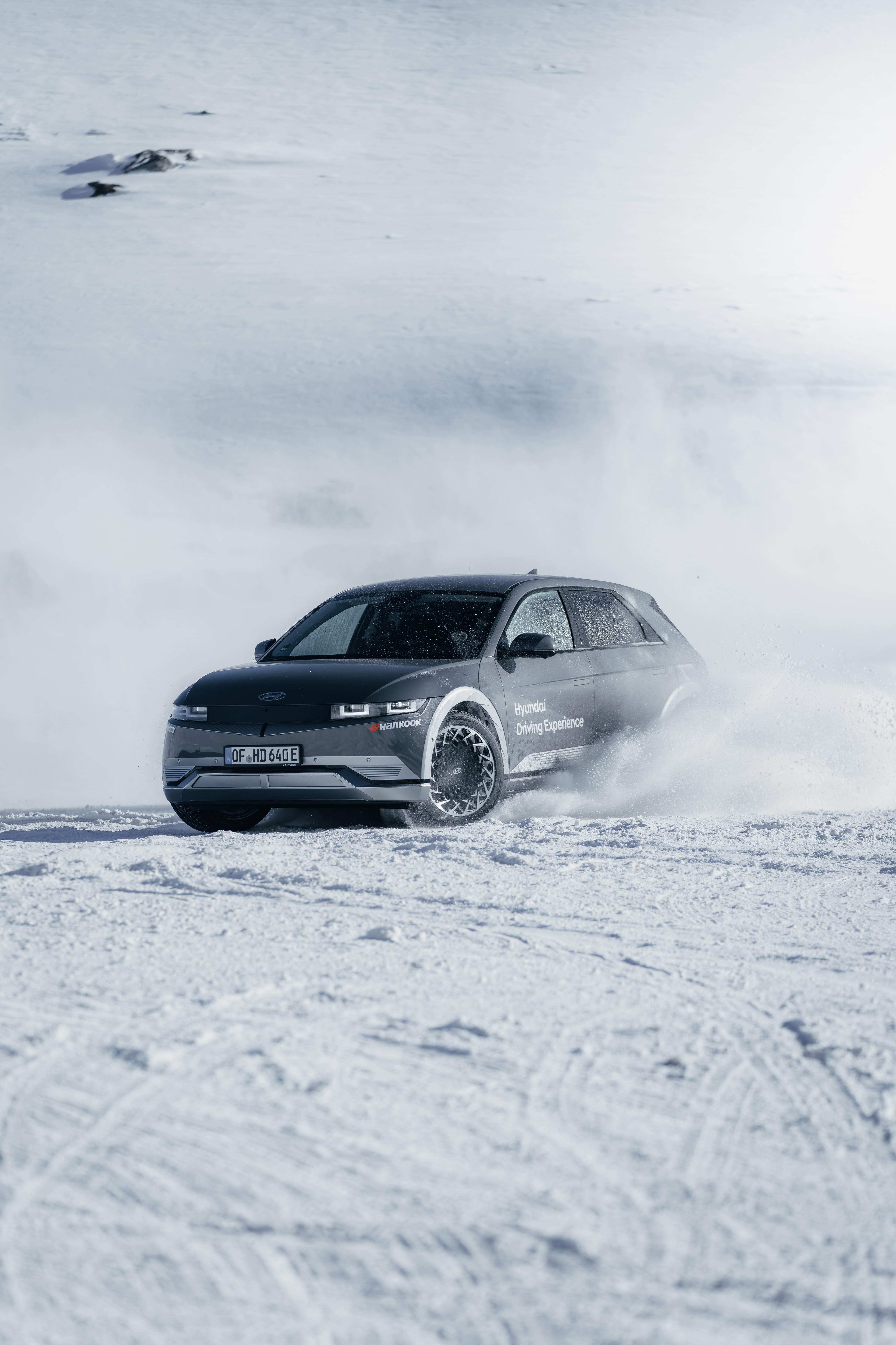 Hyundai IONIQ 5 mid-drift on the glacier, Hyundai Driving Experience livery, snow spray off studded tires