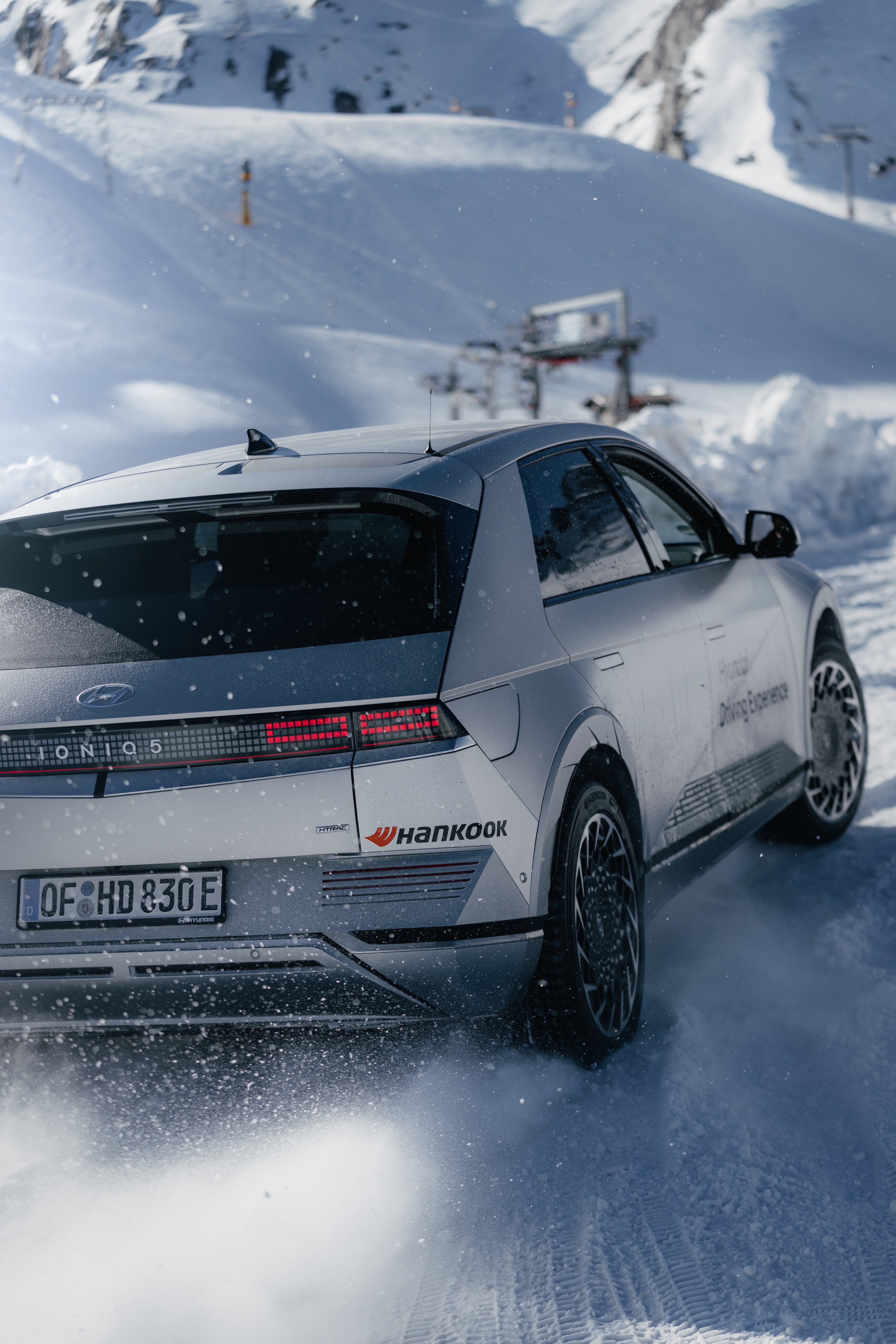 Hyundai IONIQ 5 rear three-quarter on the glacier, ski lift behind, Hyundai Driving Experience livery