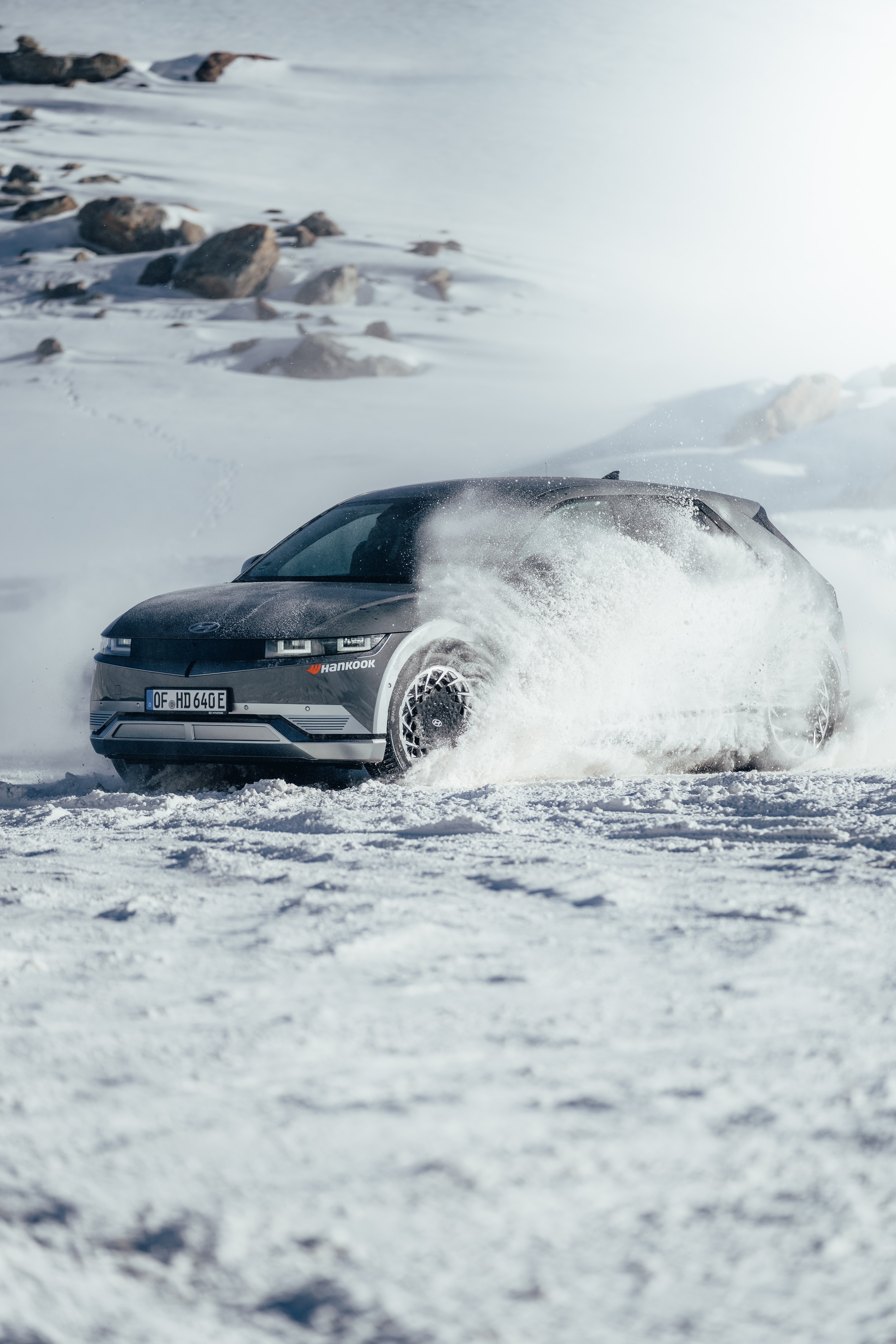 Hyundai IONIQ 5 front three-quarter drift, snow fanning across the glacier