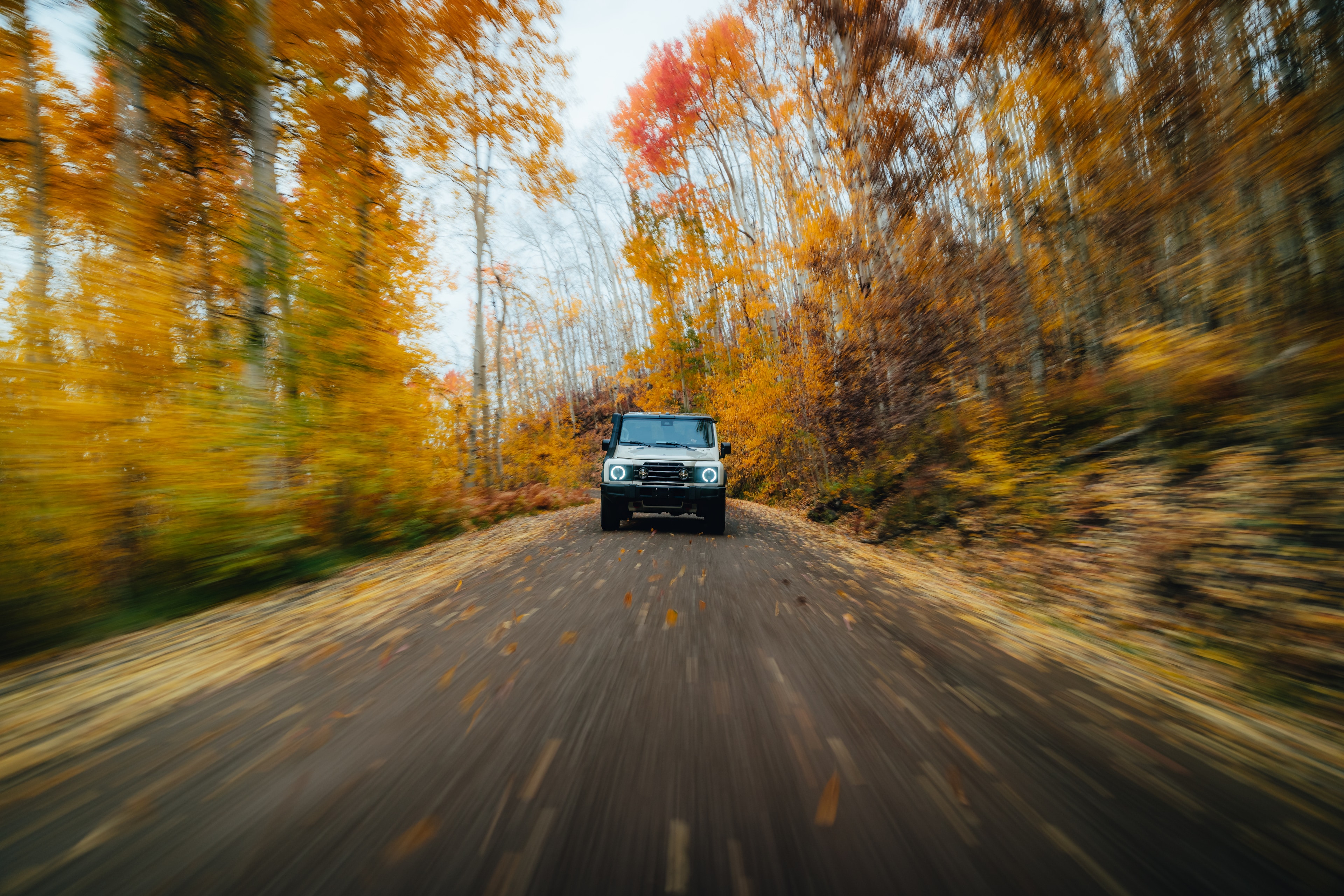 INEOS Grenadier Quartermaster in motion down a golden aspen road, leaves flying