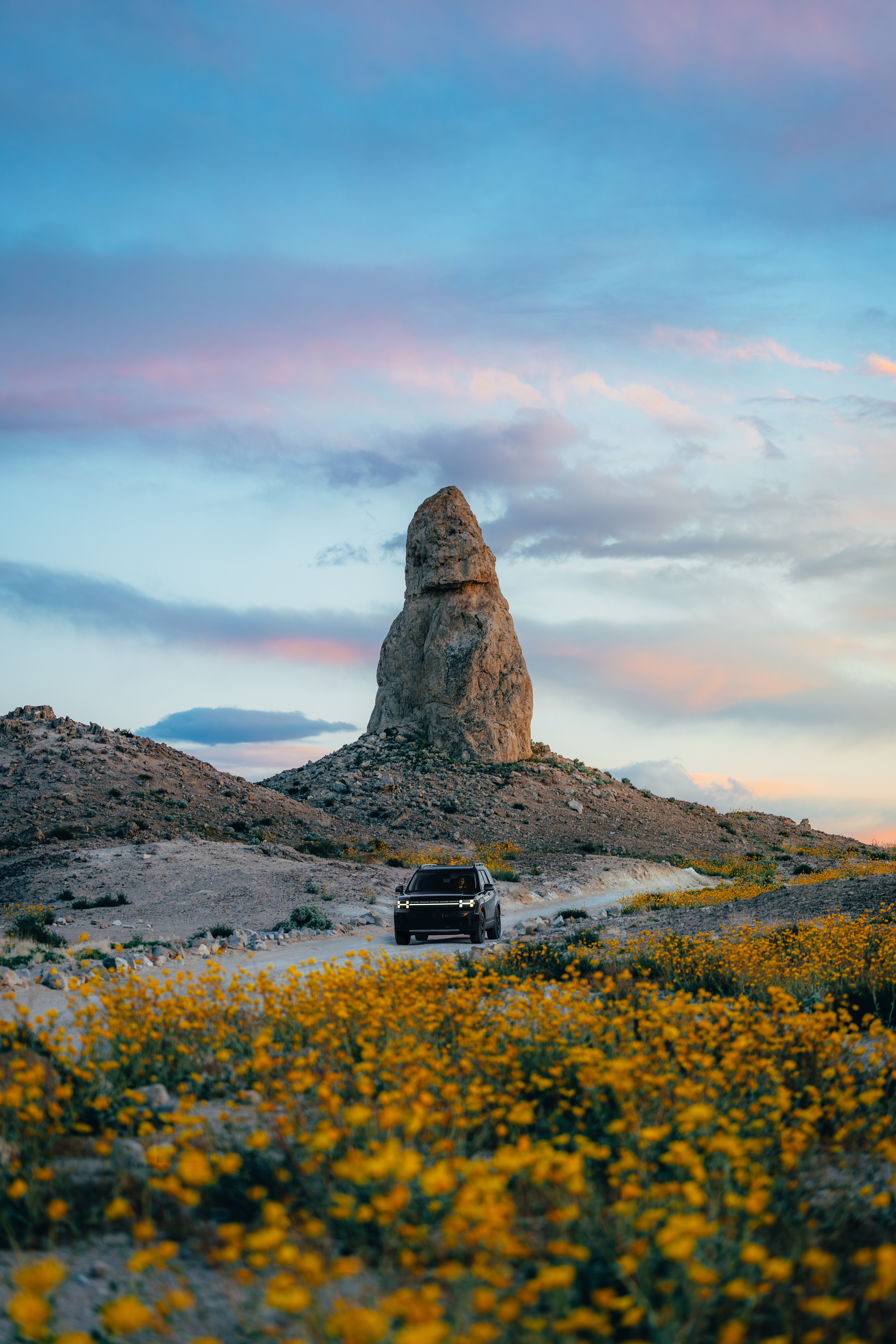 Hyundai Santa Fe beneath a tall rock spire at pastel sunset, wildflowers in the foreground