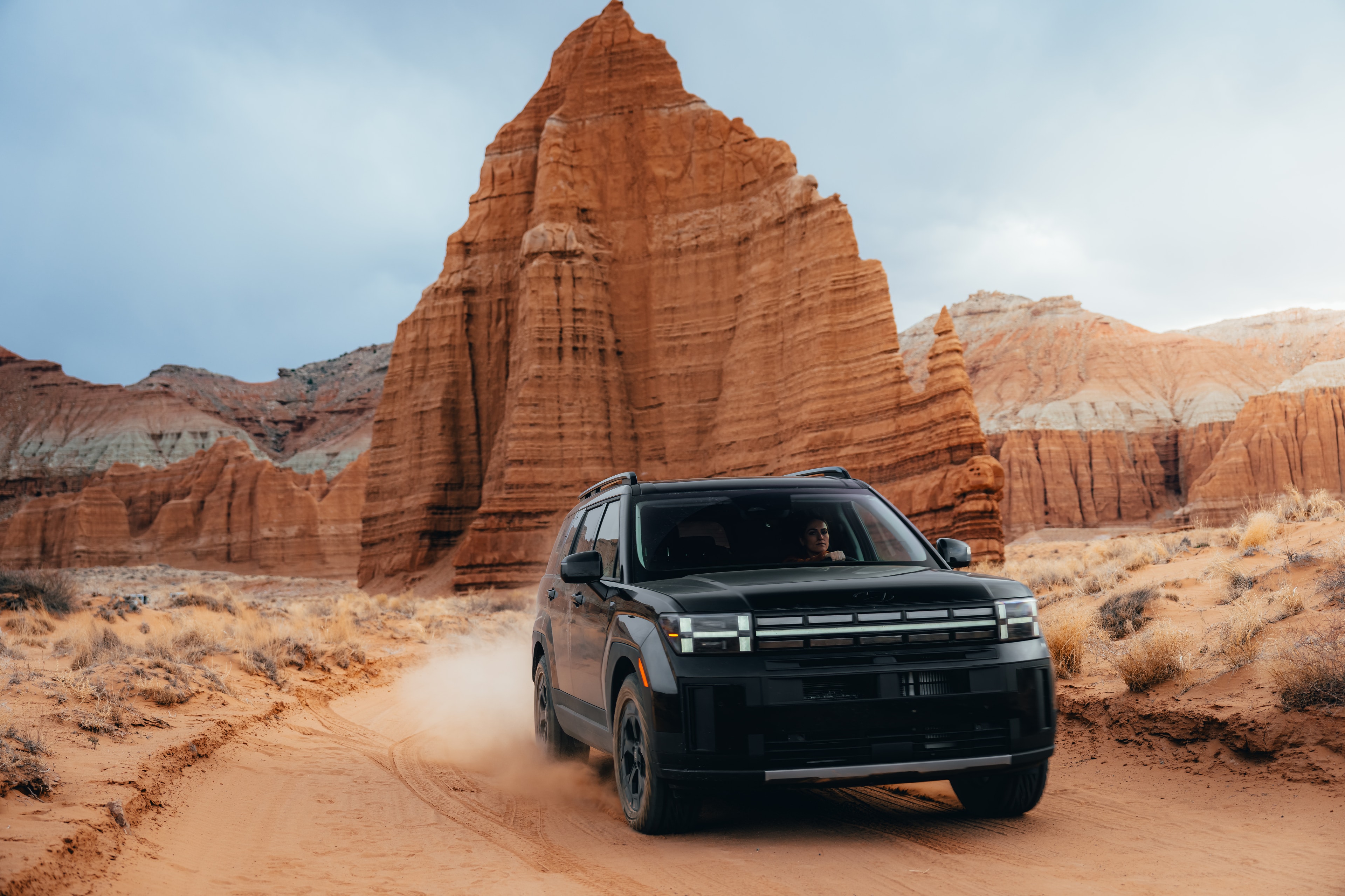 Hyundai Santa Fe kicking up dust past a red rock monolith in the Utah desert