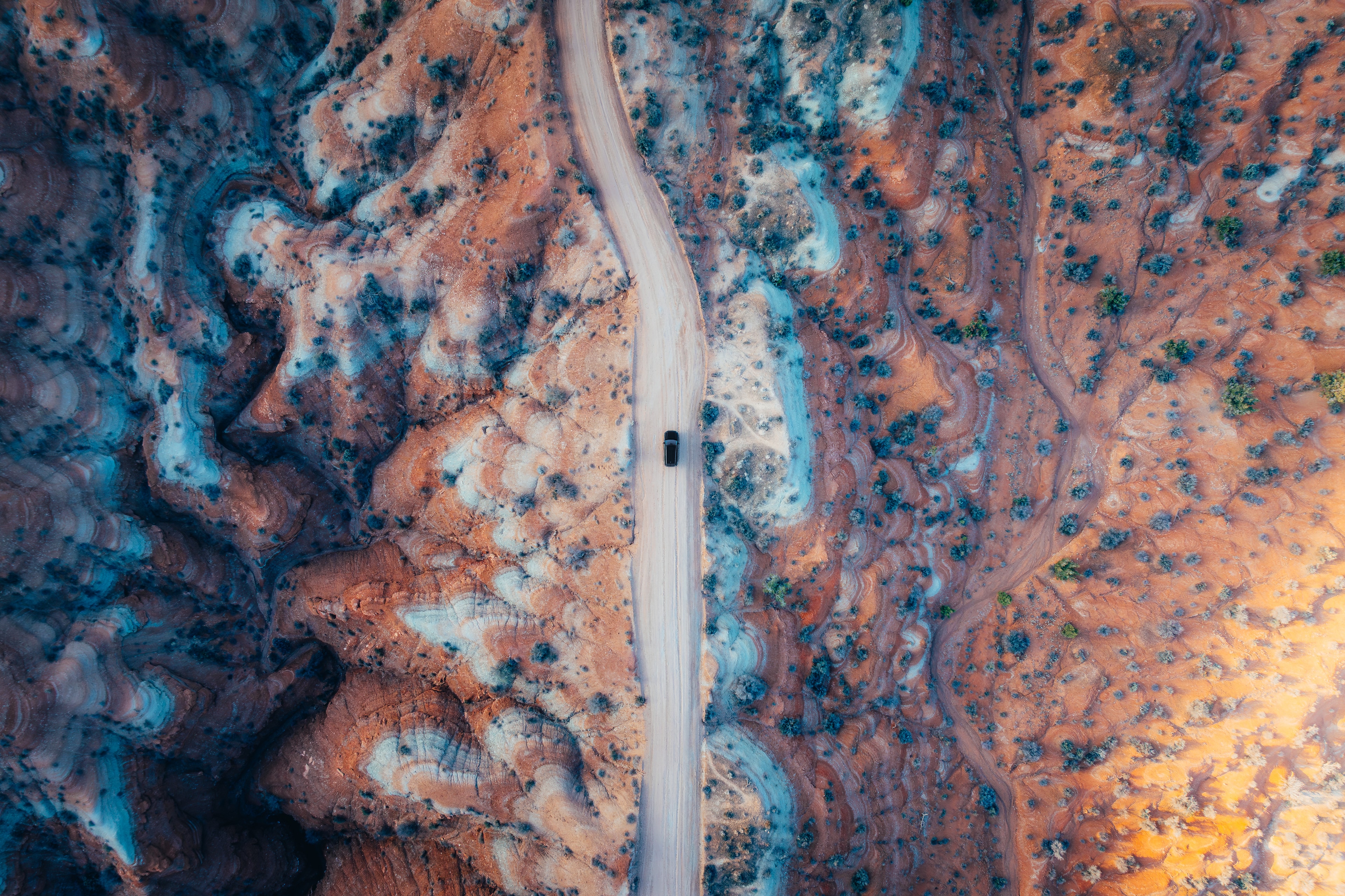 Aerial top-down of the Santa Fe on a pale road through blue and red marbled badlands