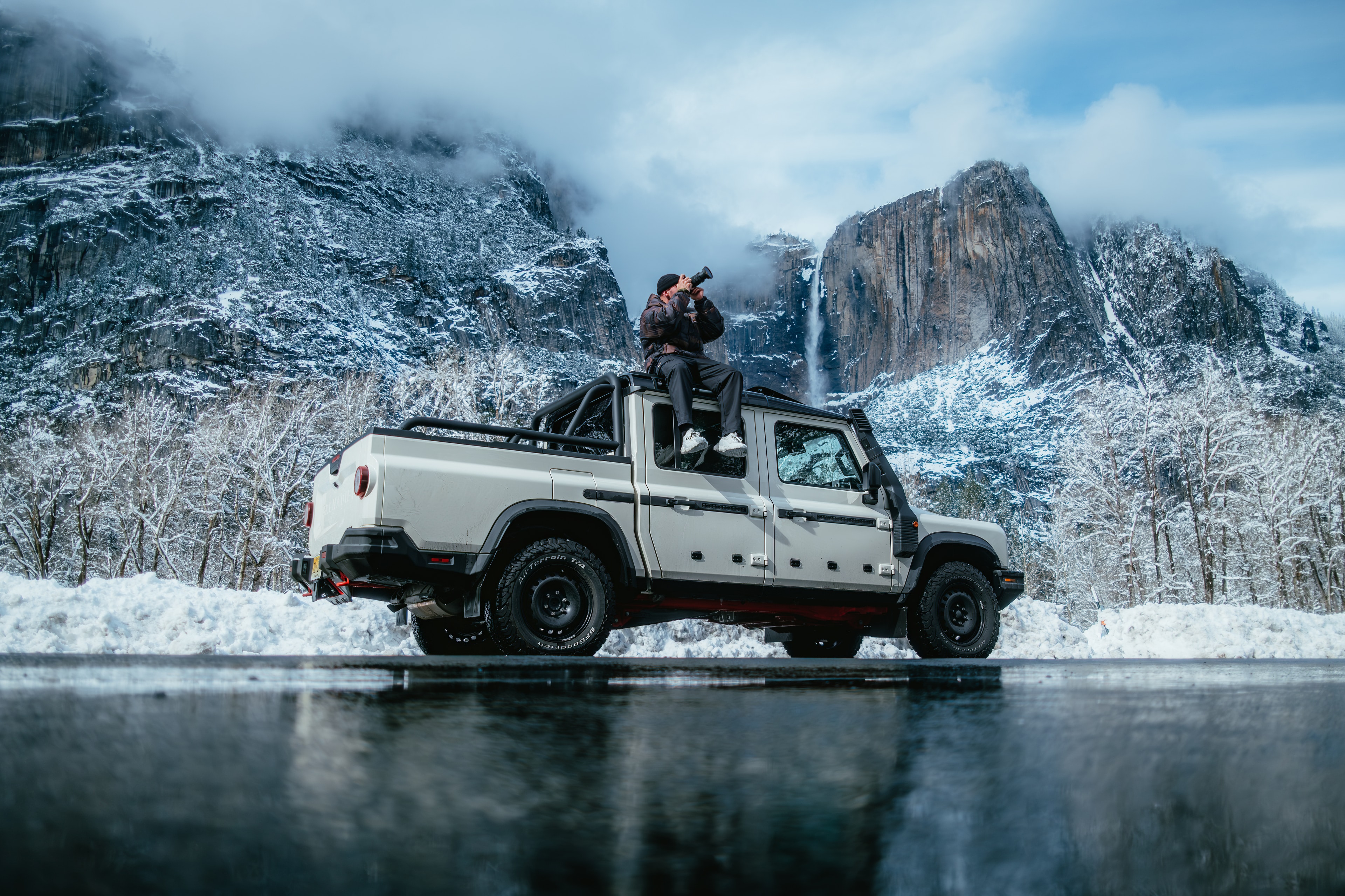 INEOS Grenadier Quartermaster beside a frozen lake reflecting Yosemite Falls, a photographer shooting from the roof