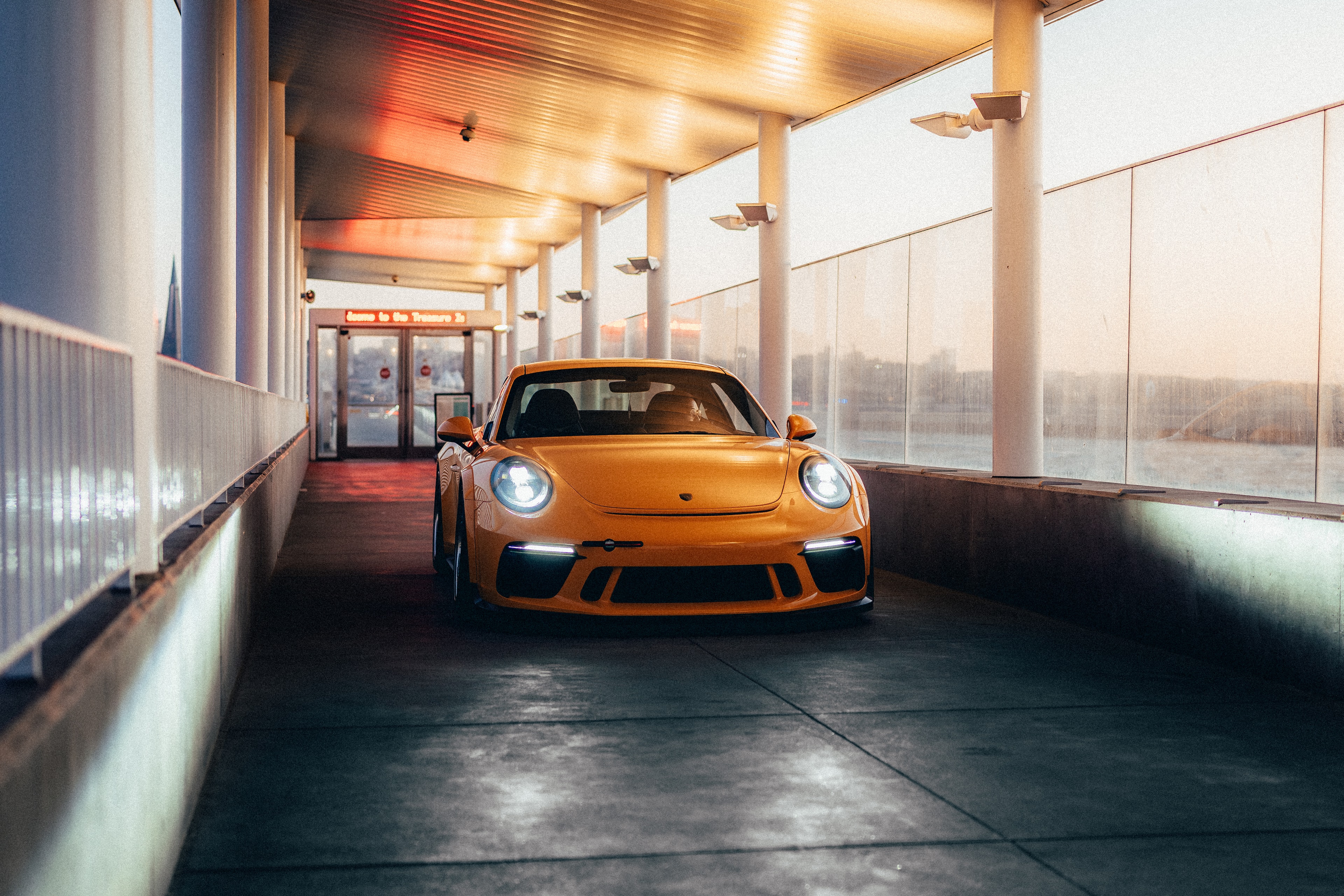 Yellow Porsche 911 GT3 head-on under the Treasure Island terminal walkway at golden hour