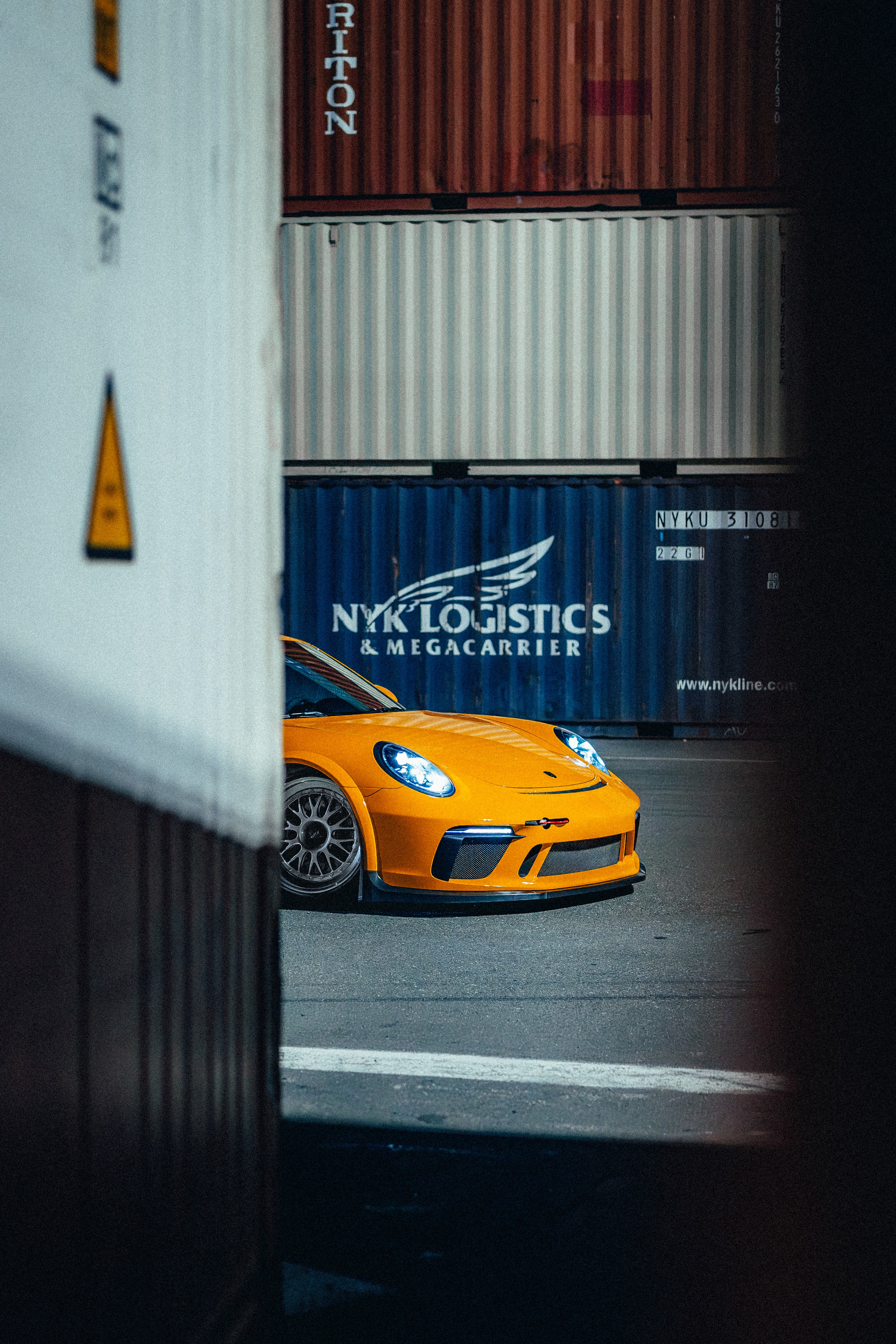 911 GT3 framed between shipping containers at night, NYK Logistics visible