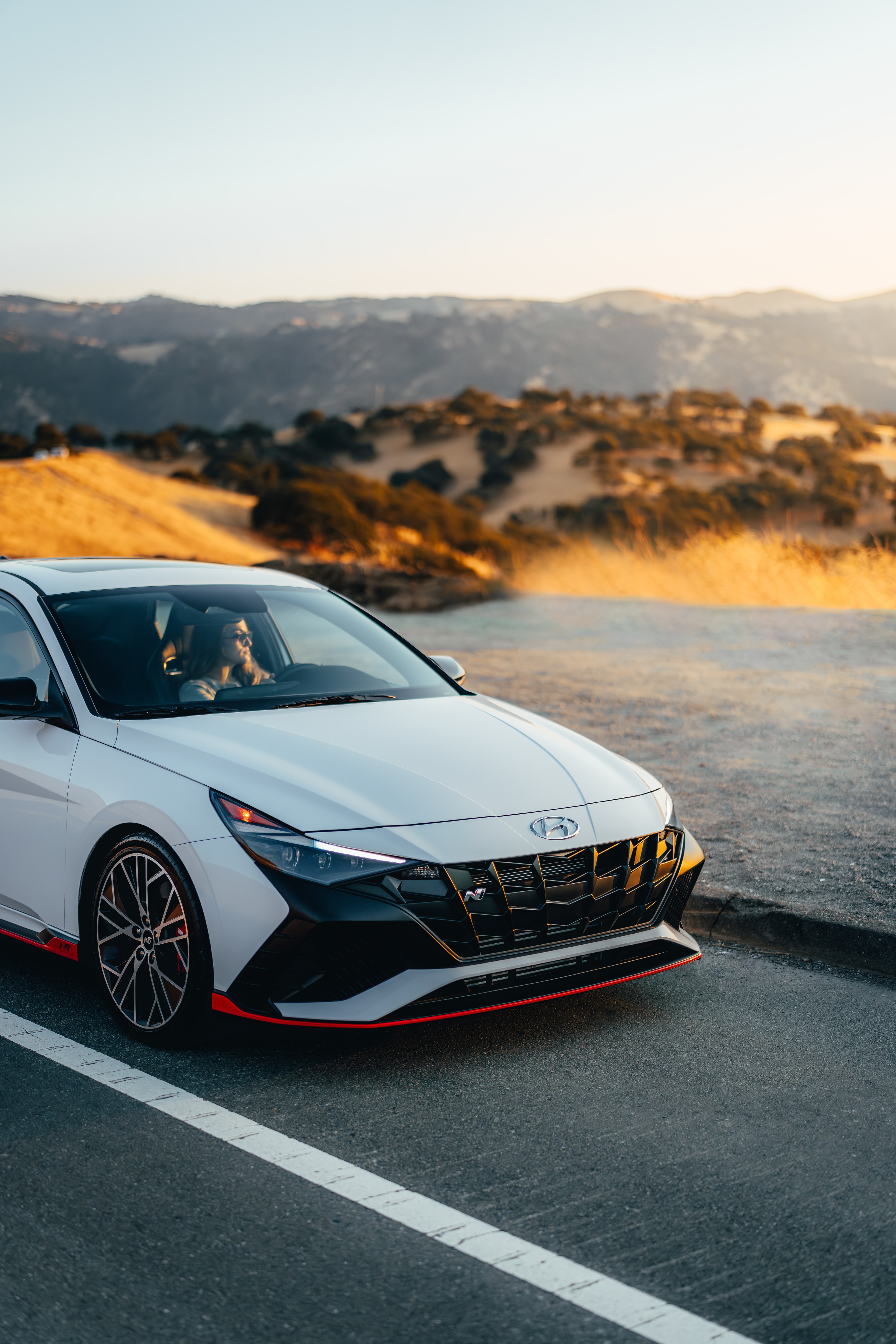 Hyundai Elantra N parked on a hilltop pullout at golden hour, driver in the seat