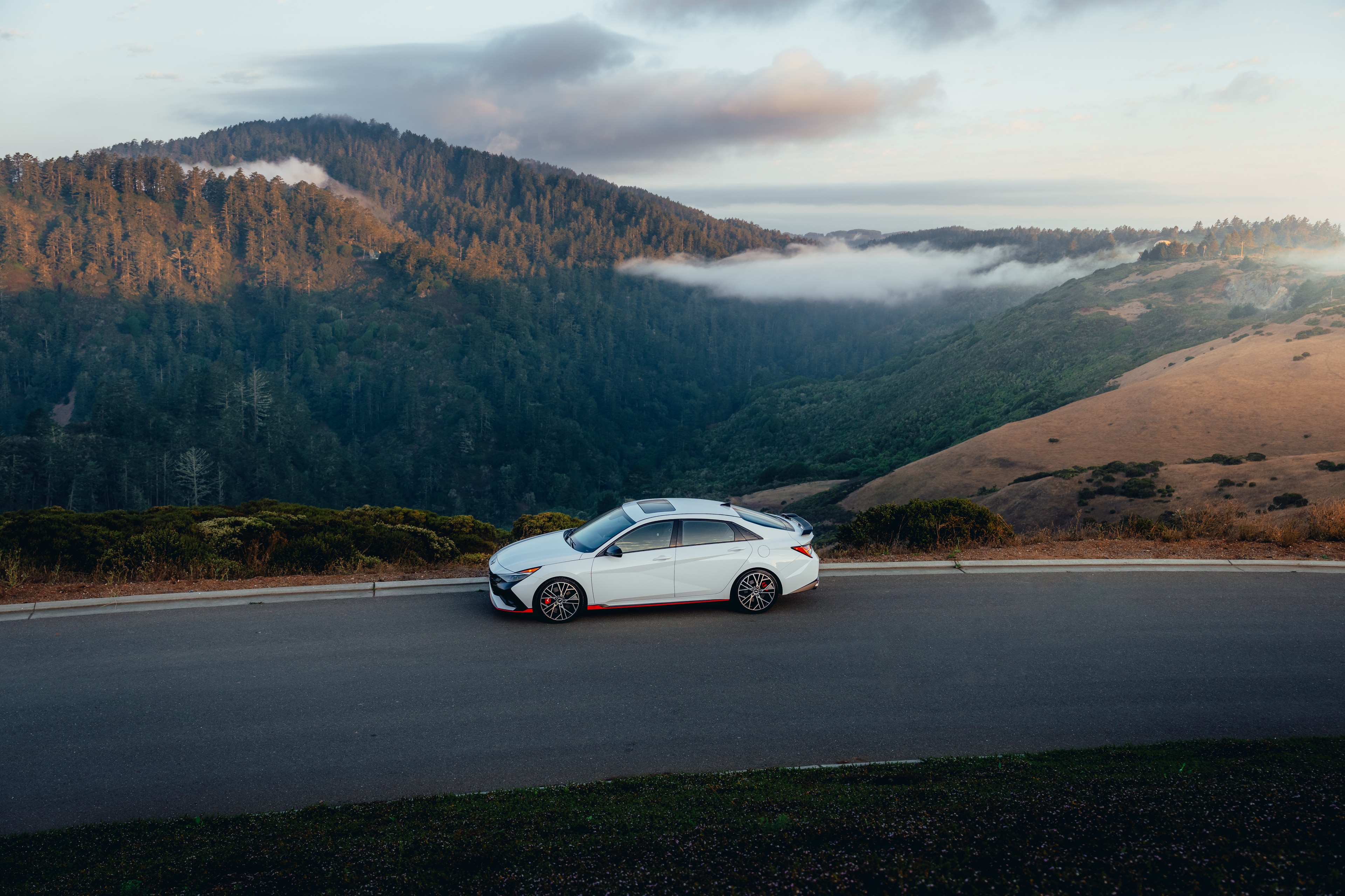 Hyundai Elantra N side profile at a coastal overlook, fog rolling over forested hills