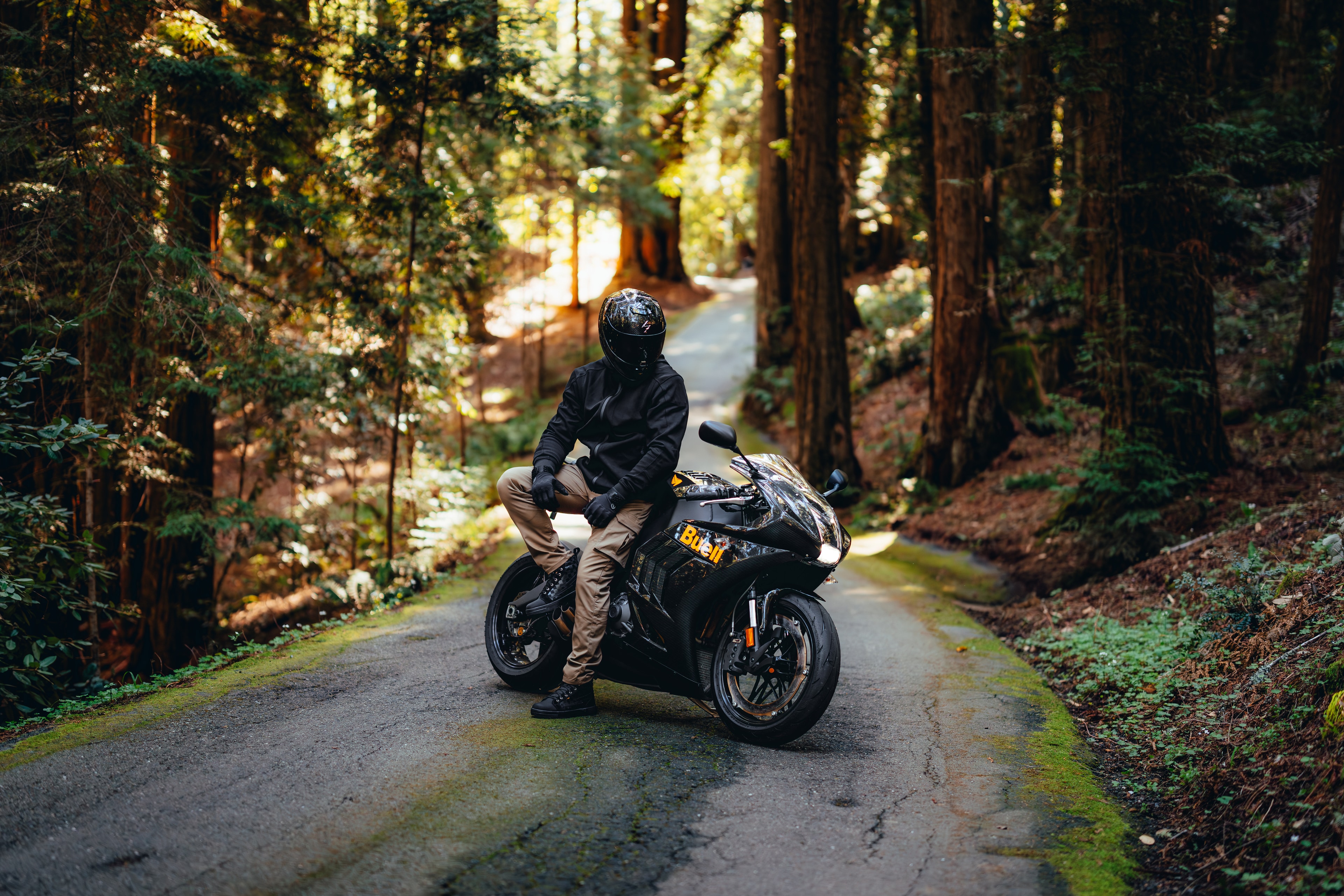 Rider sitting on the faired Buell on a backlit redwood road