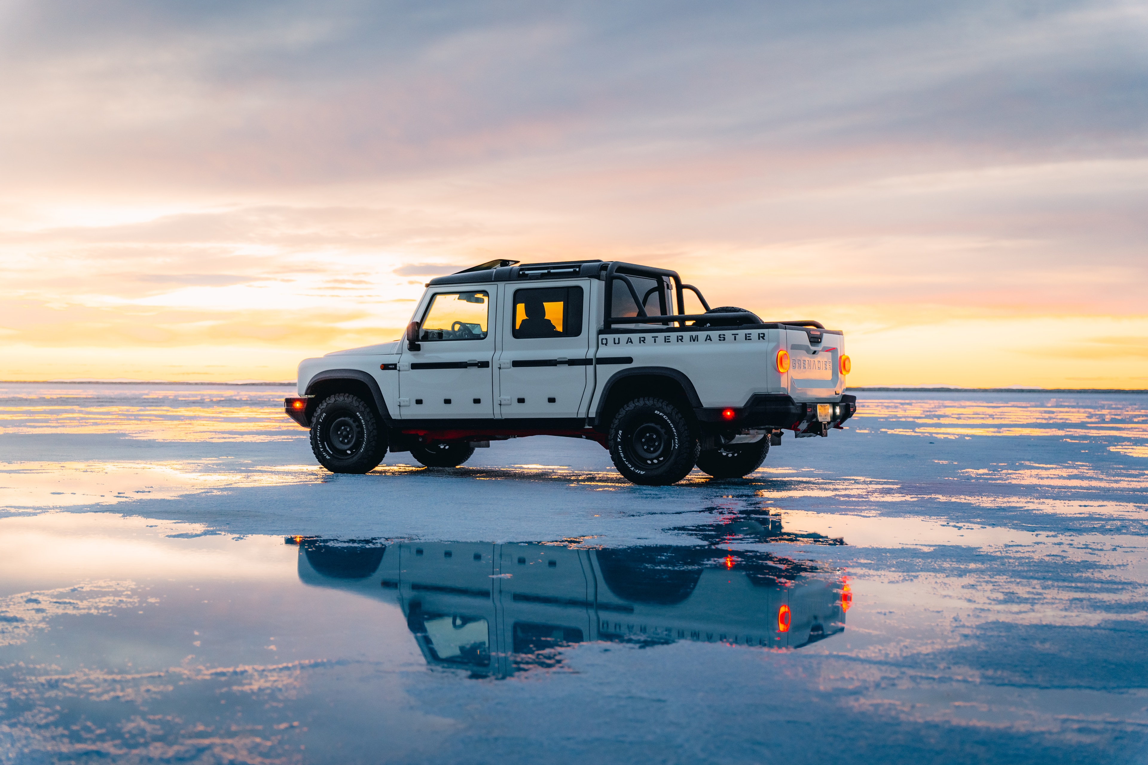INEOS Grenadier Quartermaster side profile on the wet salt flats, full reflection, pastel sunset