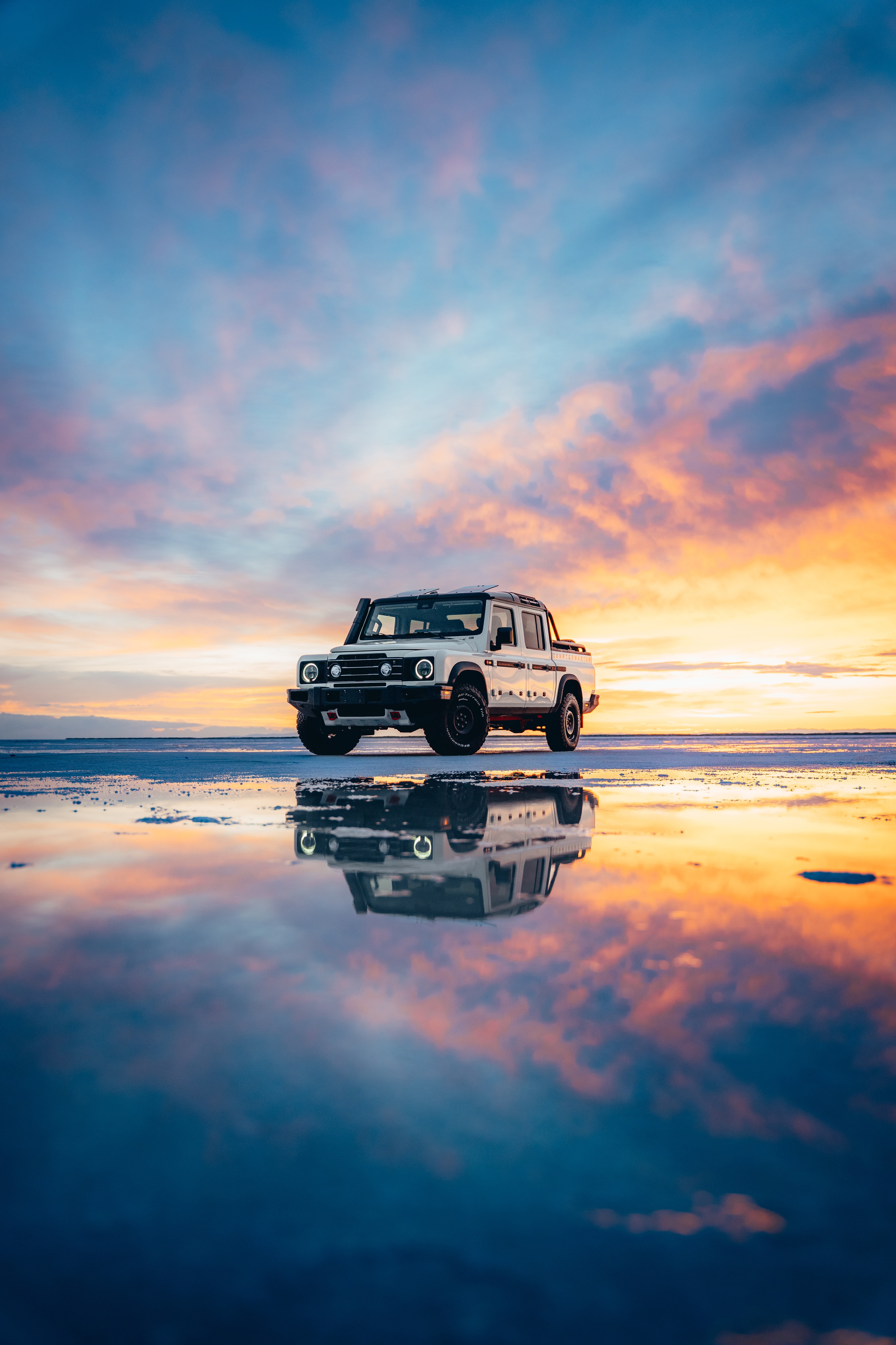 INEOS Grenadier Quartermaster head-on on the salt flats, a fiery sky mirrored below