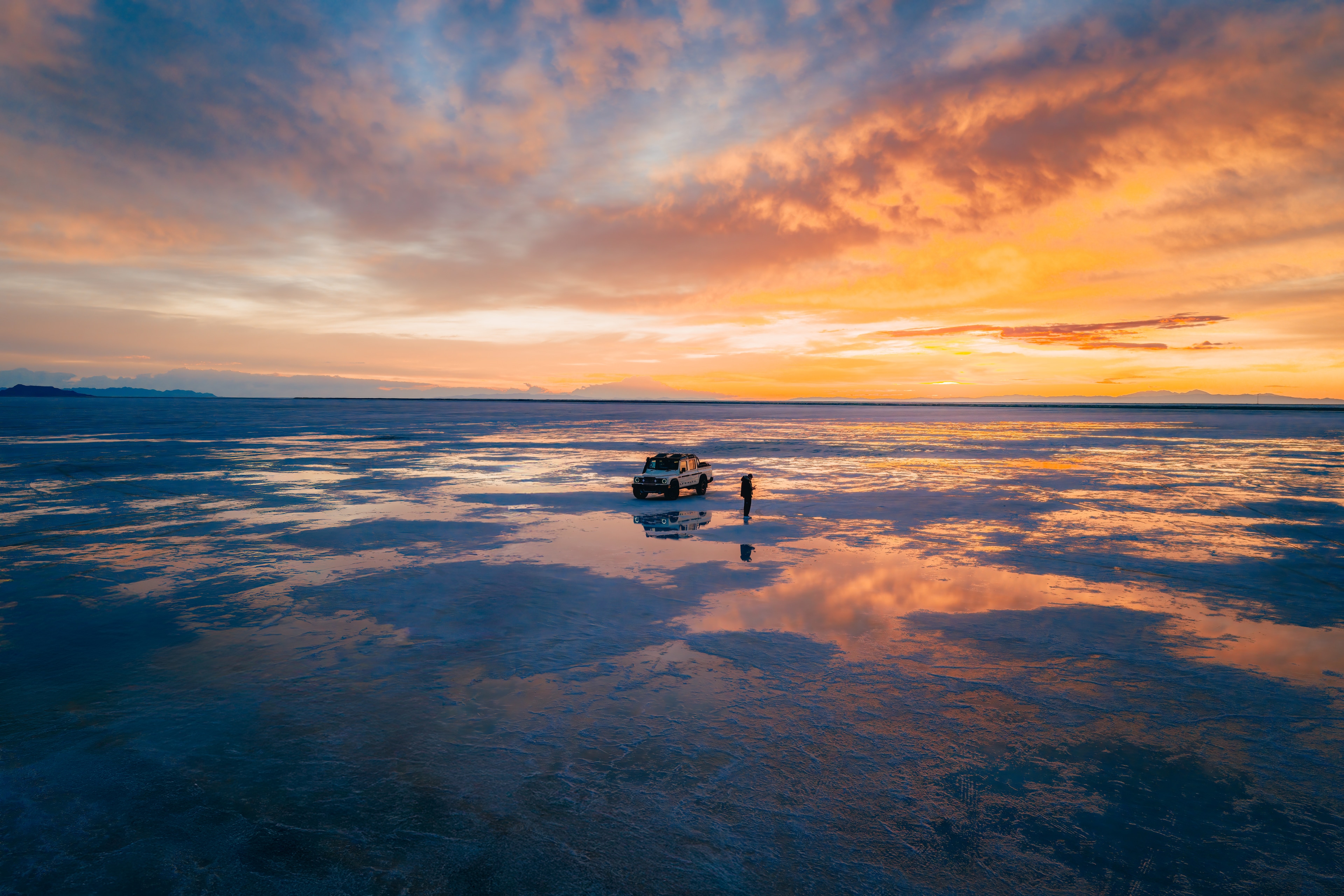 INEOS Grenadier Quartermaster alone on the vast Bonneville salt flats at fiery sunset, mirrored in the wet salt