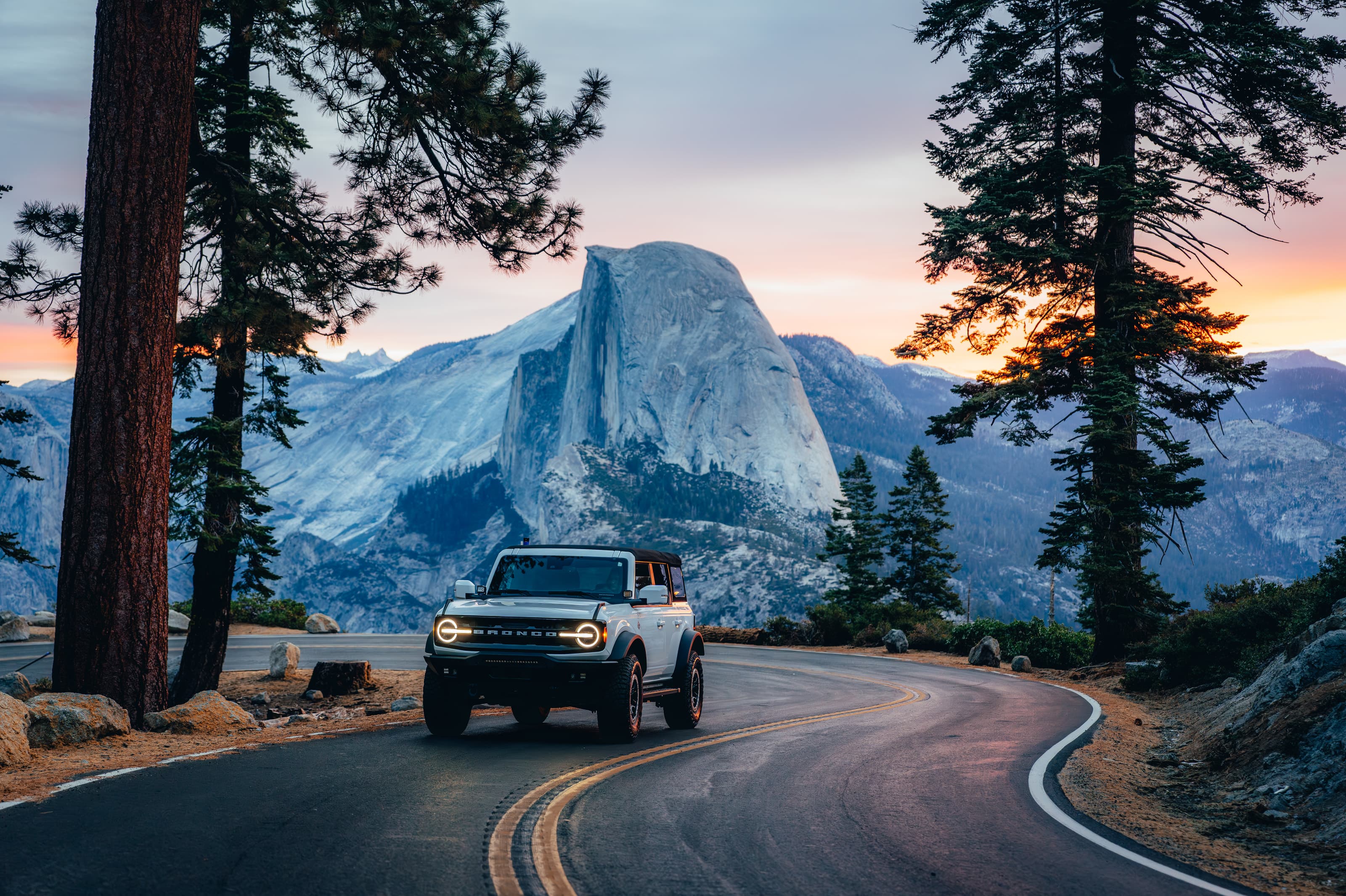 White Ford Bronco on a winding road below Half Dome at sunset, Yosemite