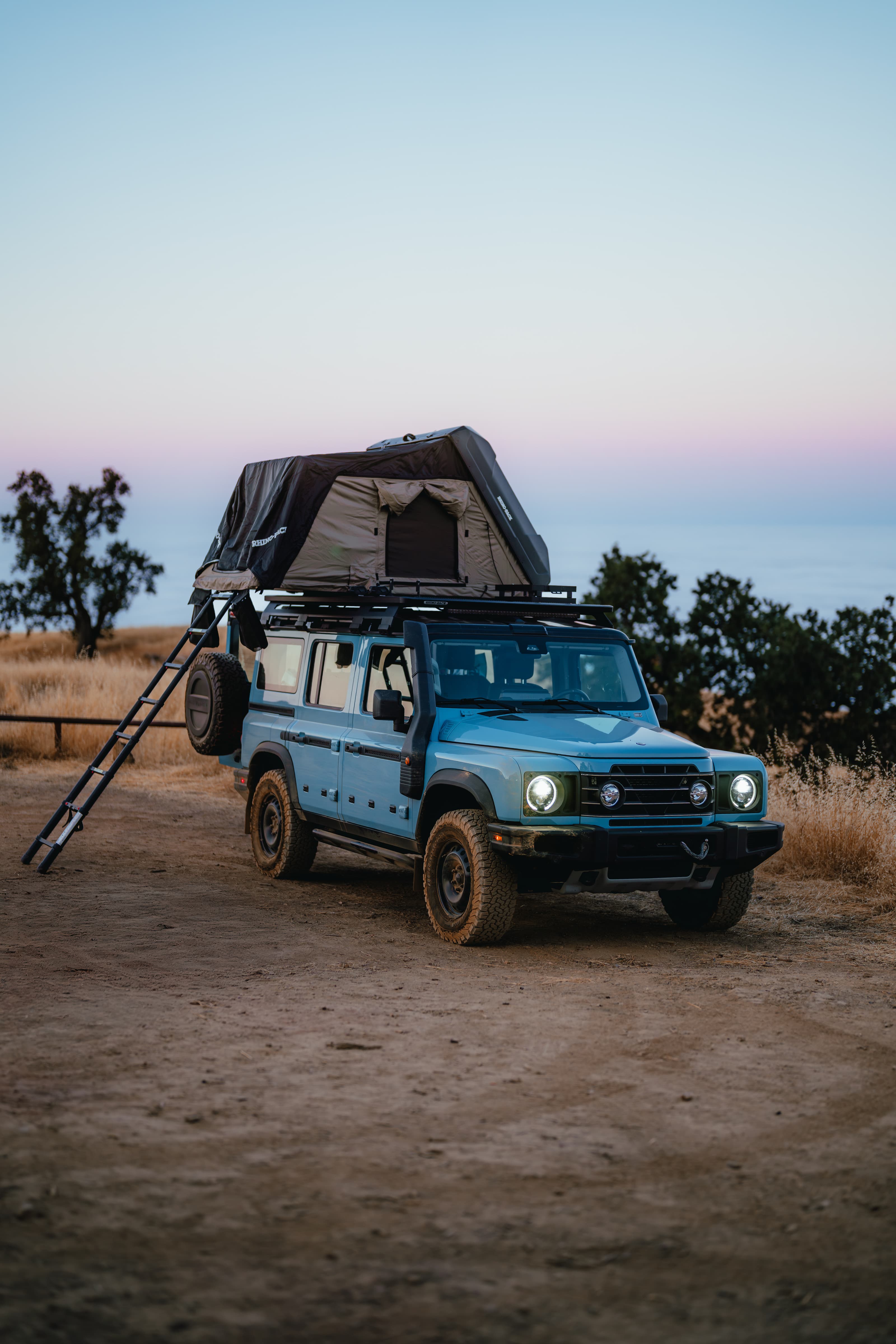 INEOS Grenadier with a rooftop tent open at a coastal camp at dusk
