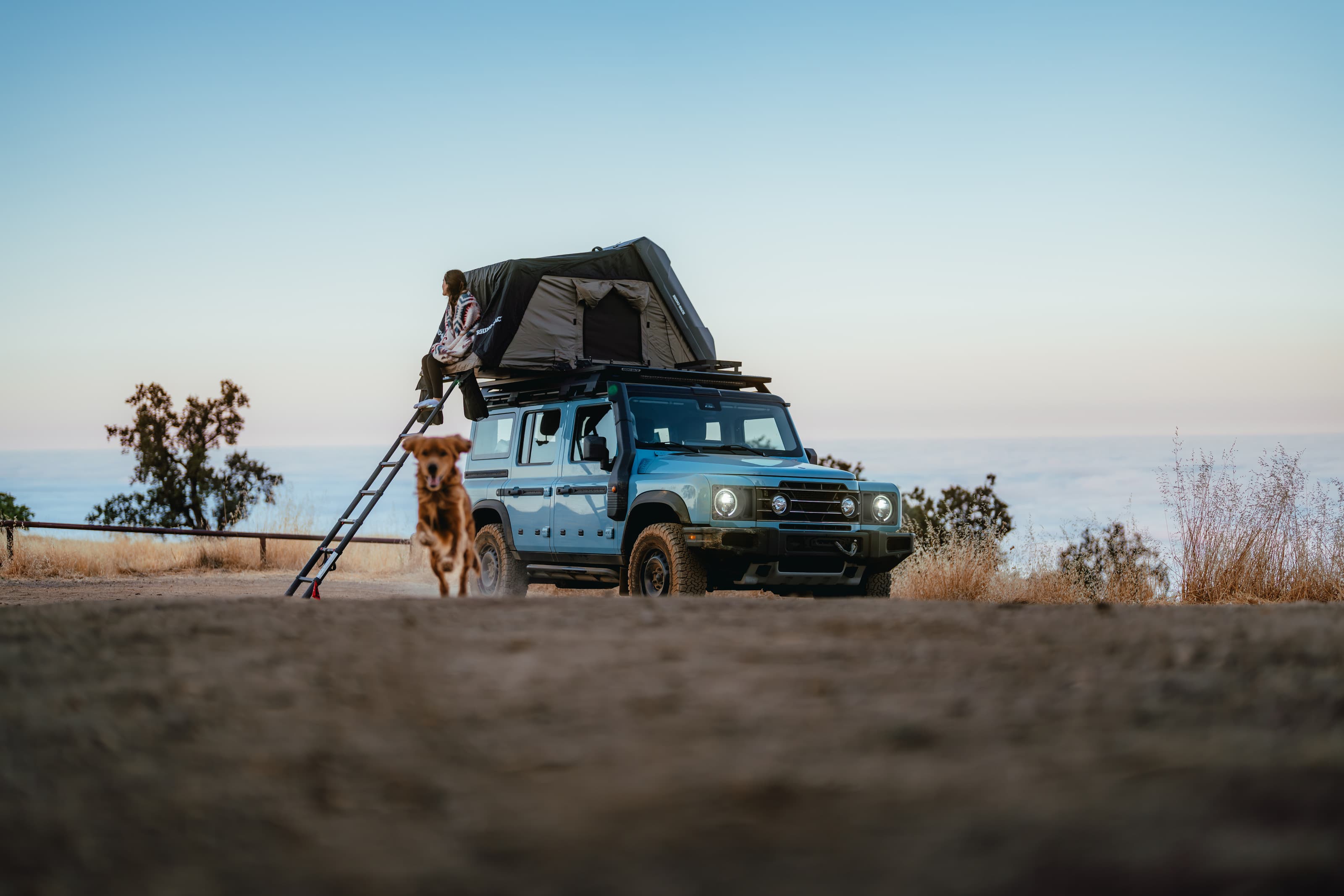 INEOS Grenadier with a rooftop tent above the marine layer, a dog alongside at dusk