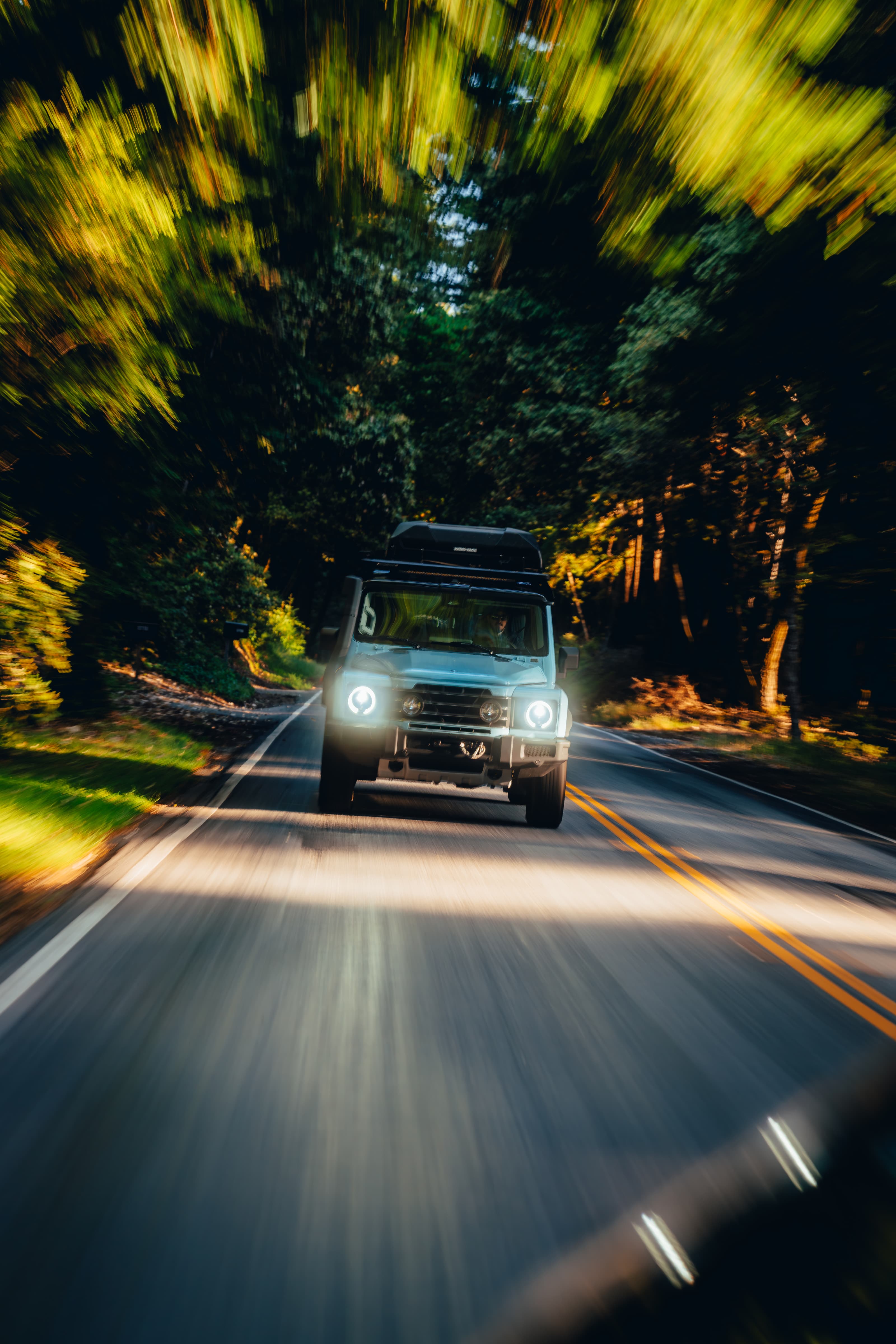 INEOS Grenadier in motion on a sunlit forest road, motion blur