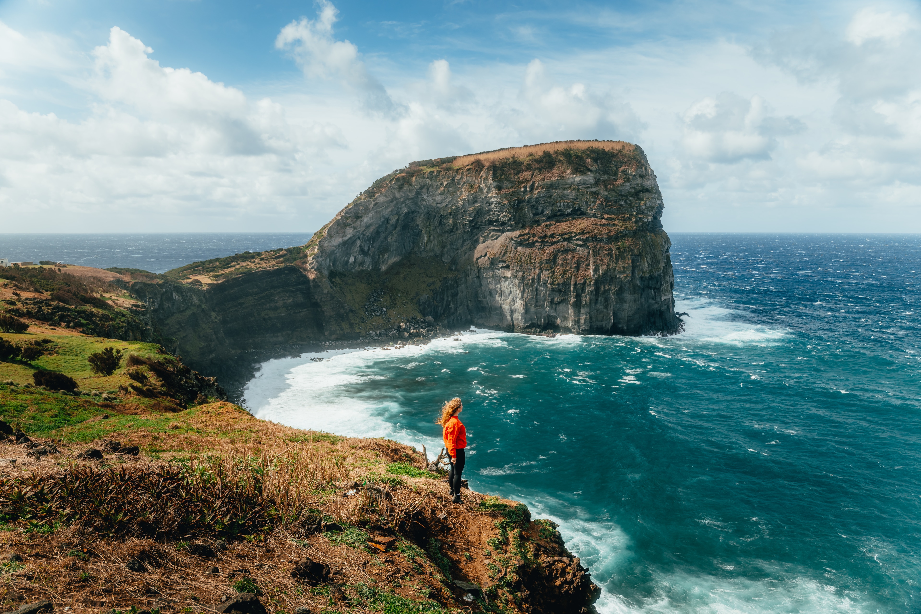 A lone figure on a sheer green sea cliff above the breaking Atlantic