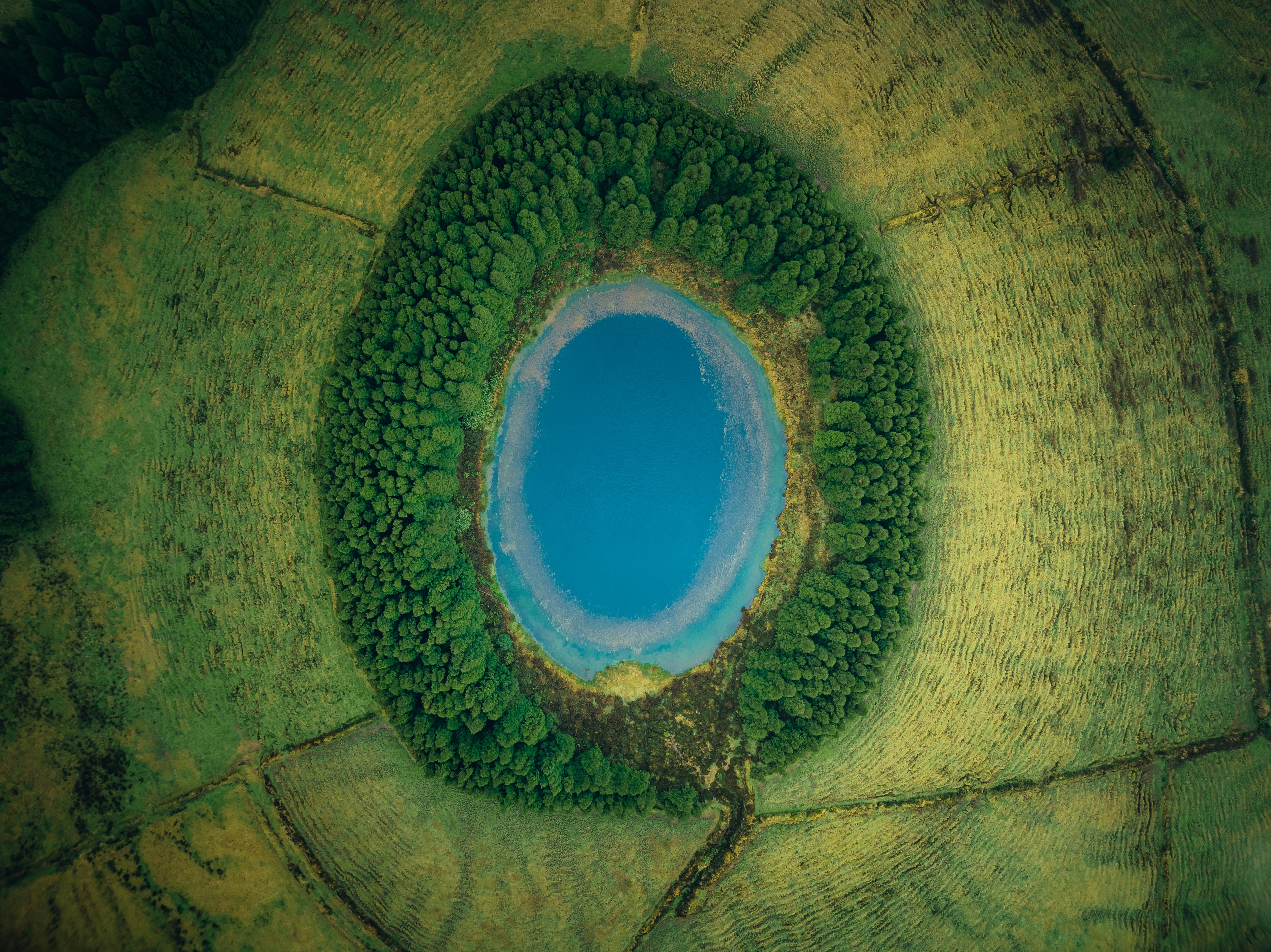 A deep blue crater lake ringed by green caldera walls, seen from above