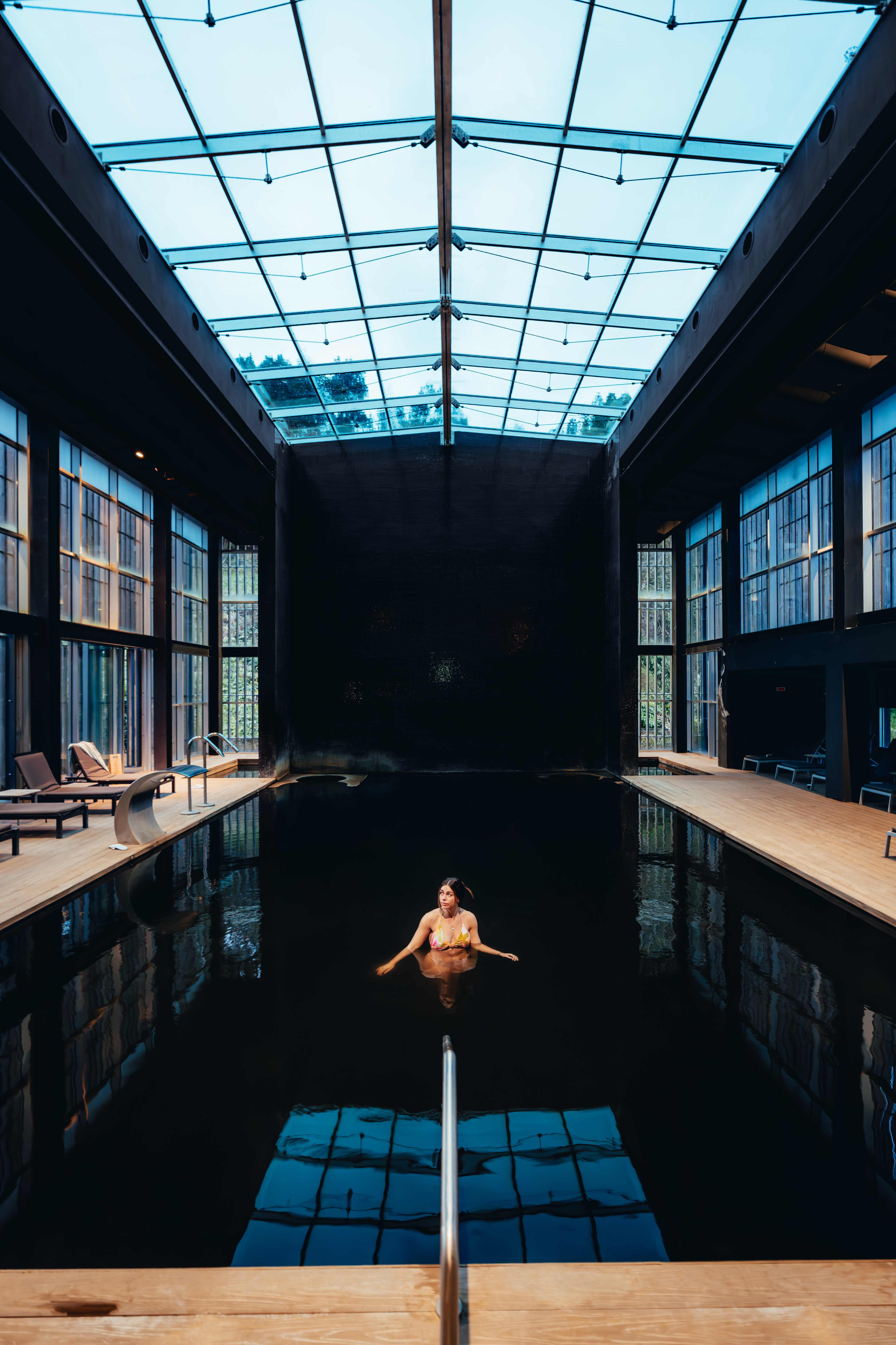 A swimmer floating in a still pool beneath a glass-roofed hall