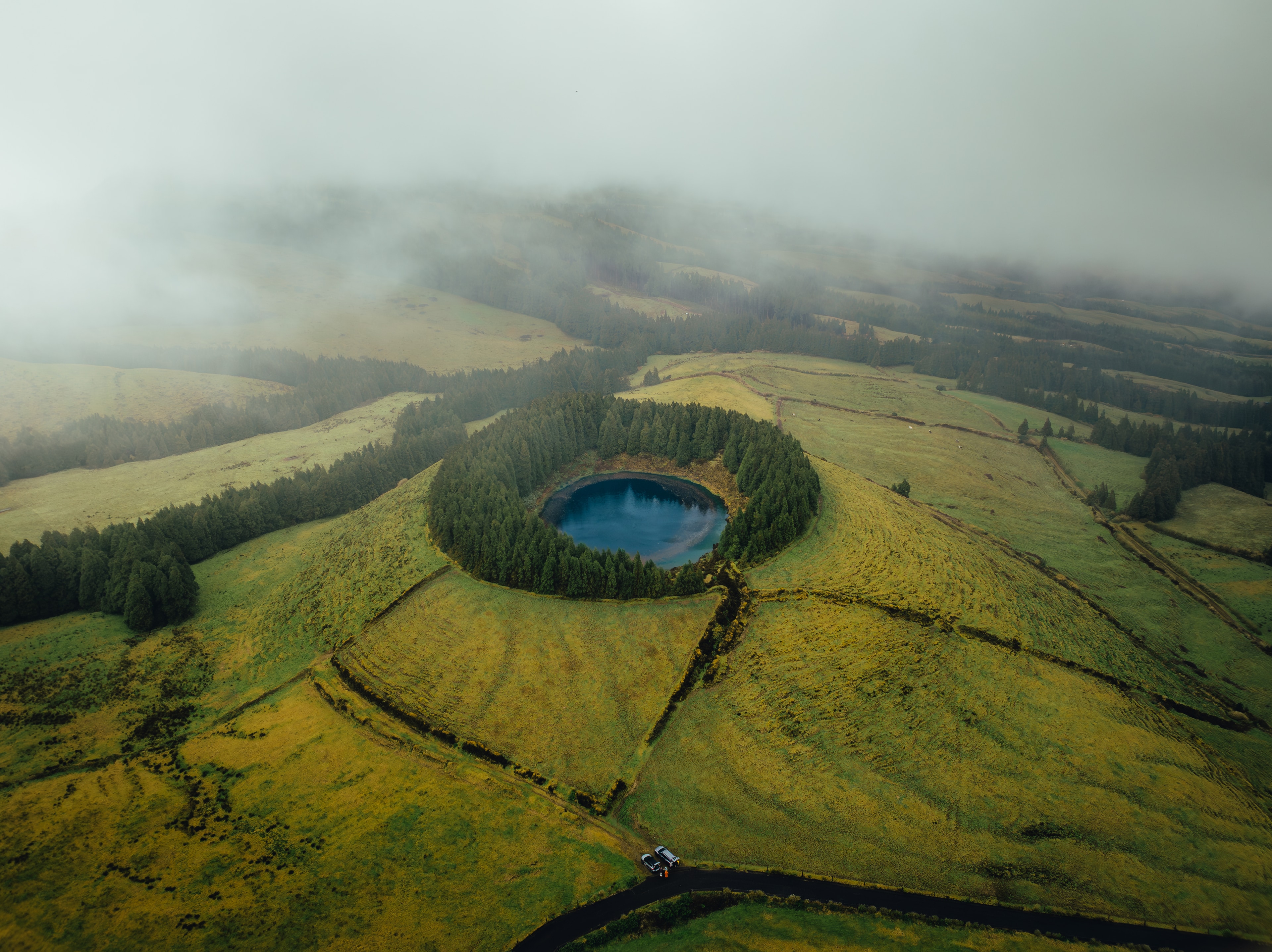 Green crater fields and a small lake under low drifting cloud, from above