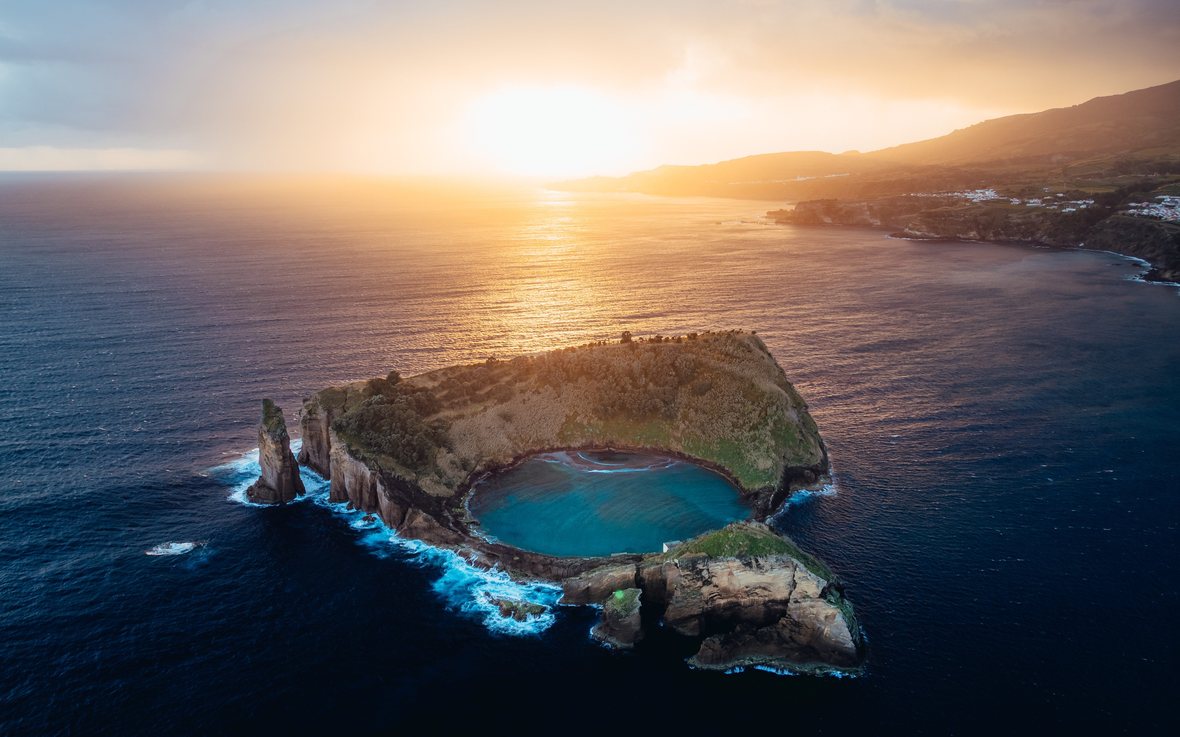 A natural sea pool inside a lava arch, glowing under a golden Atlantic sunset