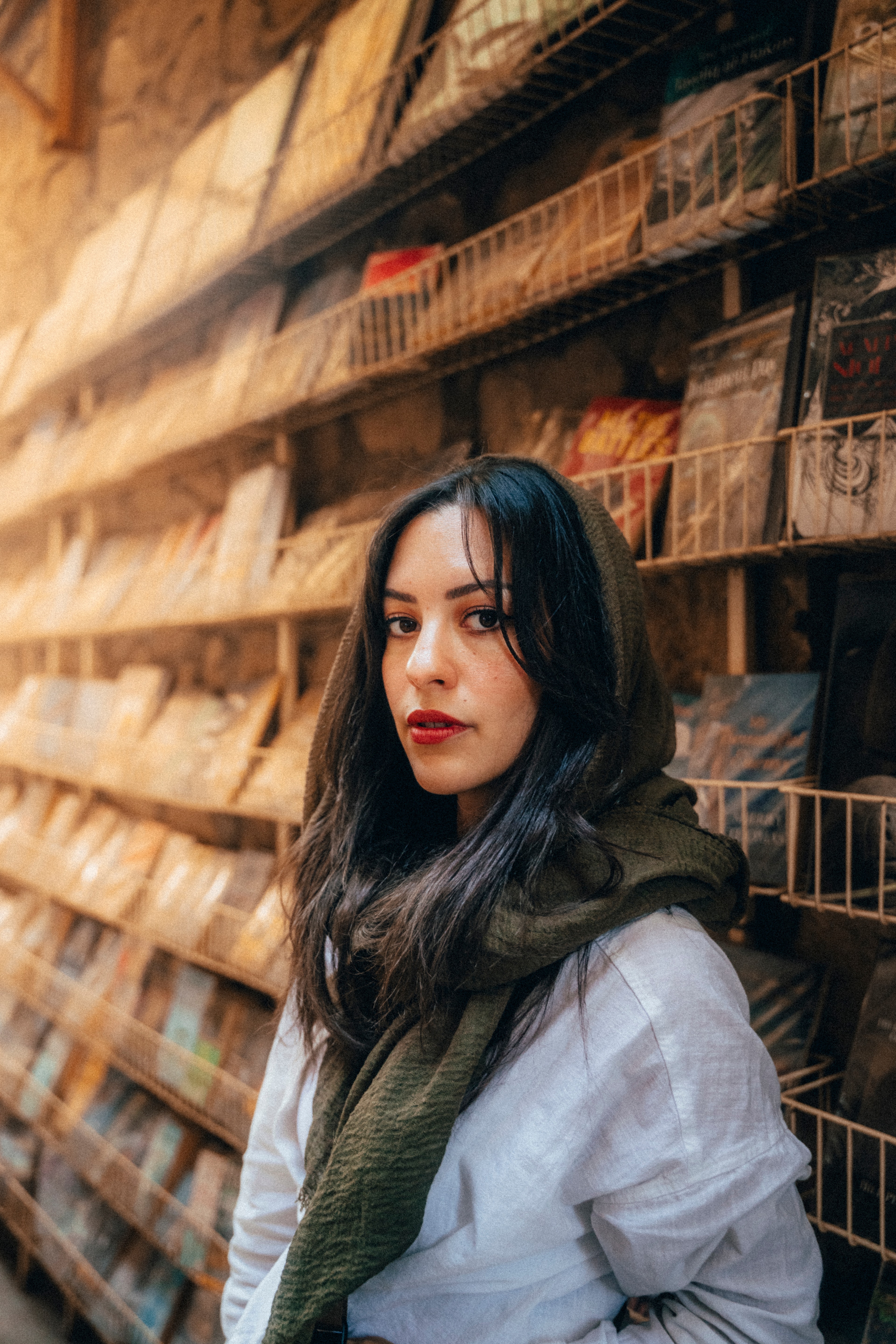 A woman in an olive scarf at a wall of wooden spice market shelves