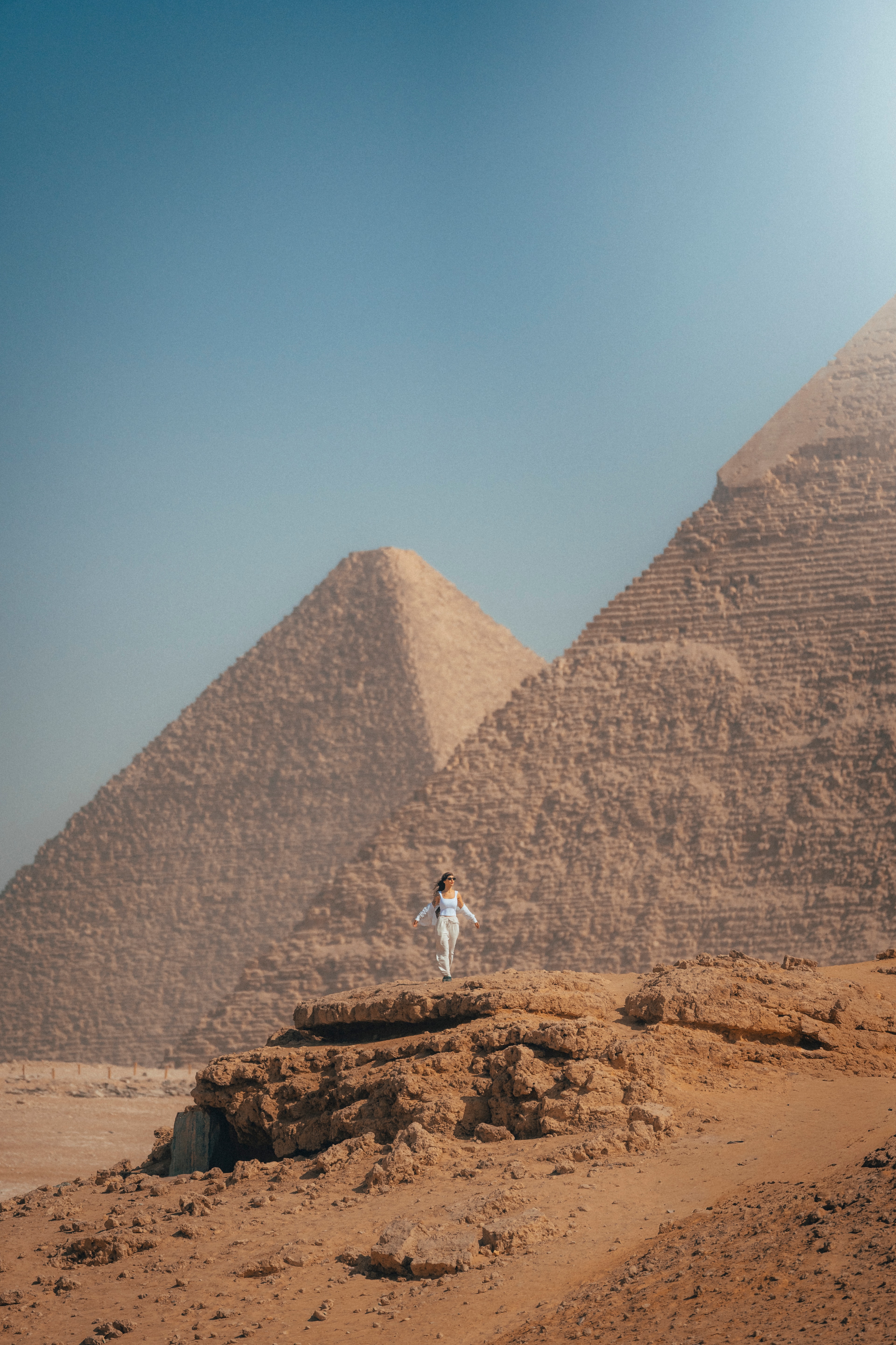 A figure in white standing on a rock outcrop, the three Giza pyramids on the horizon