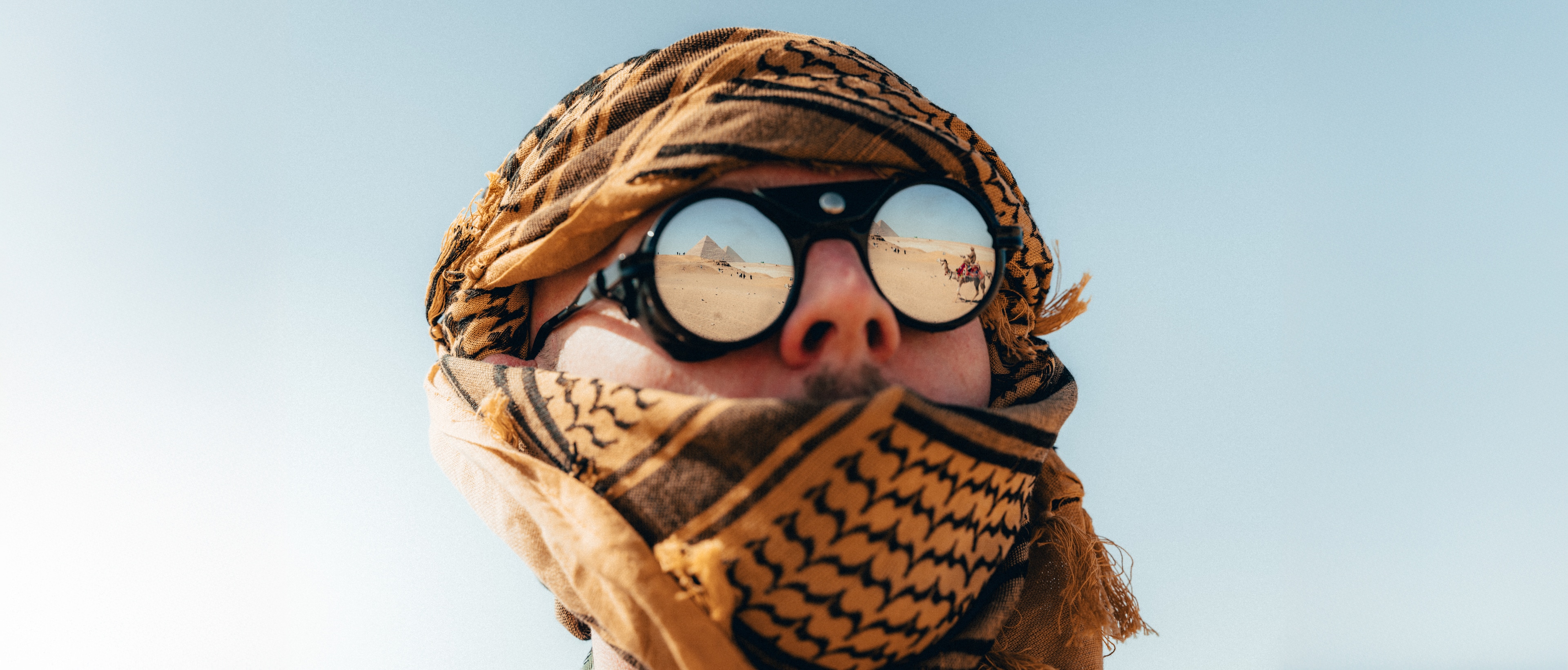 A traveler in a keffiyeh and mirrored round goggles, the Giza pyramids reflected in the lenses