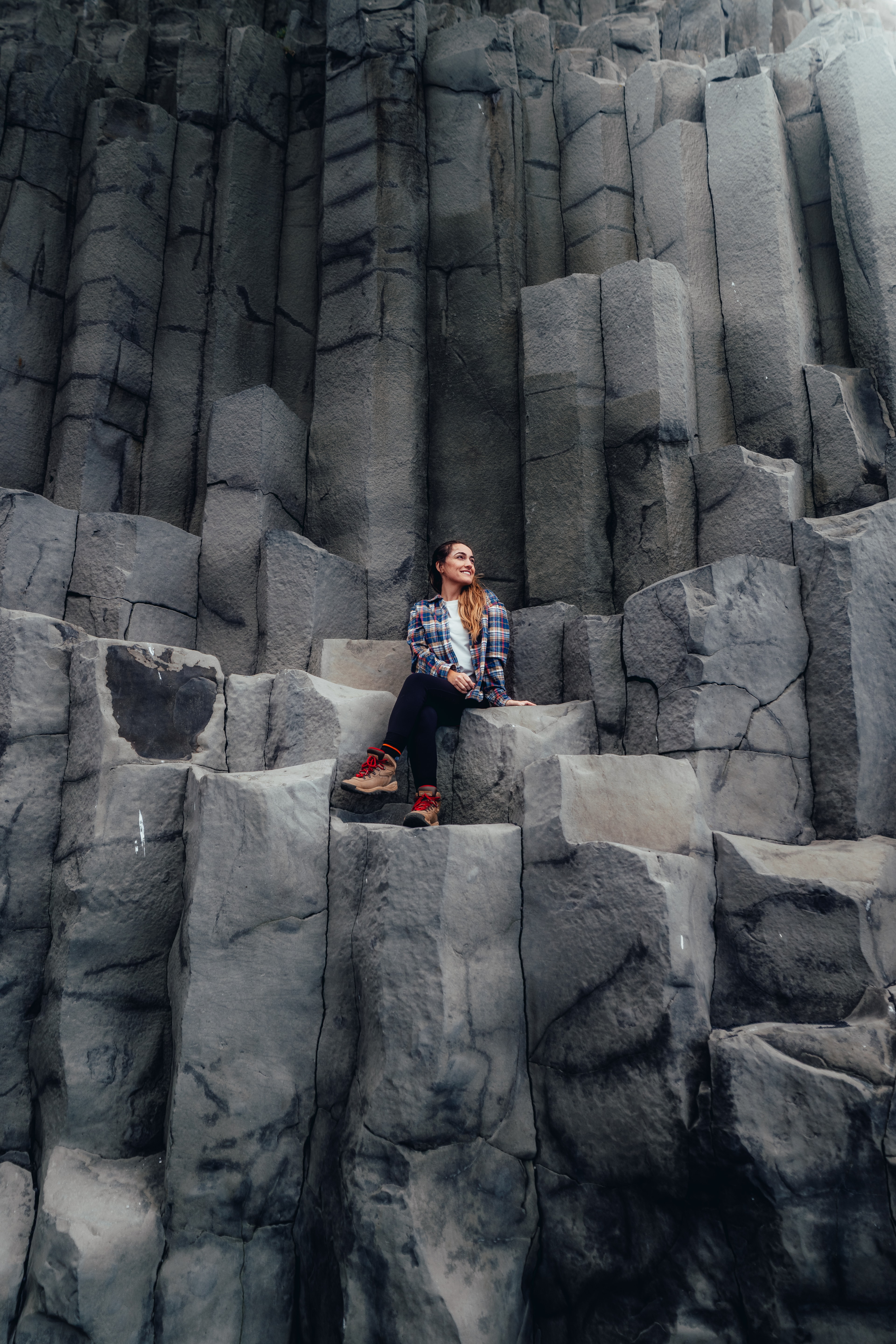 A woman in a plaid flannel resting on the basalt columns at Reynisfjara