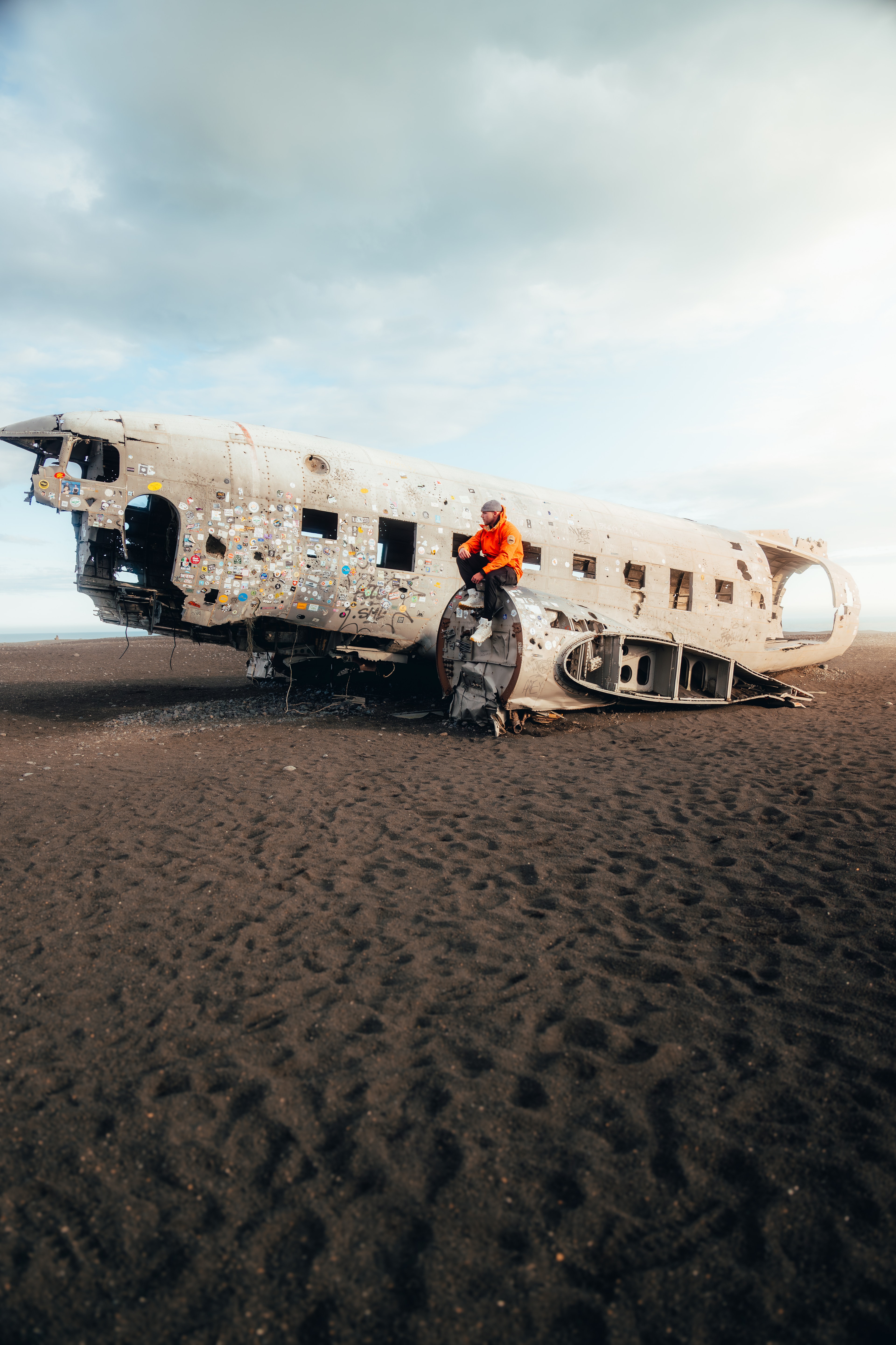 A figure in an orange shell on the wing of the DC-3 wreck on the black sand