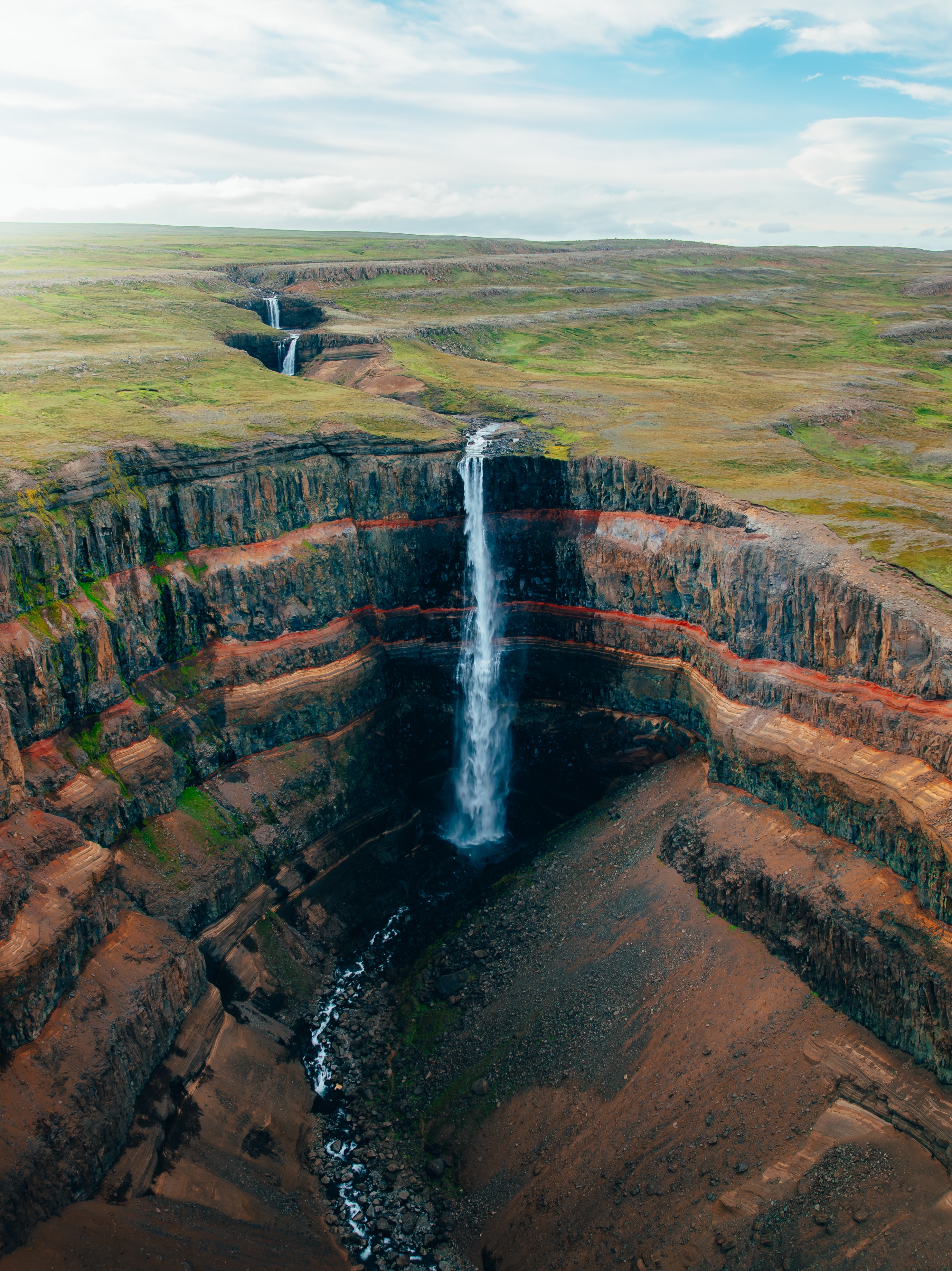 Aerial view of Hengifoss falling down a deep red-and-black banded canyon