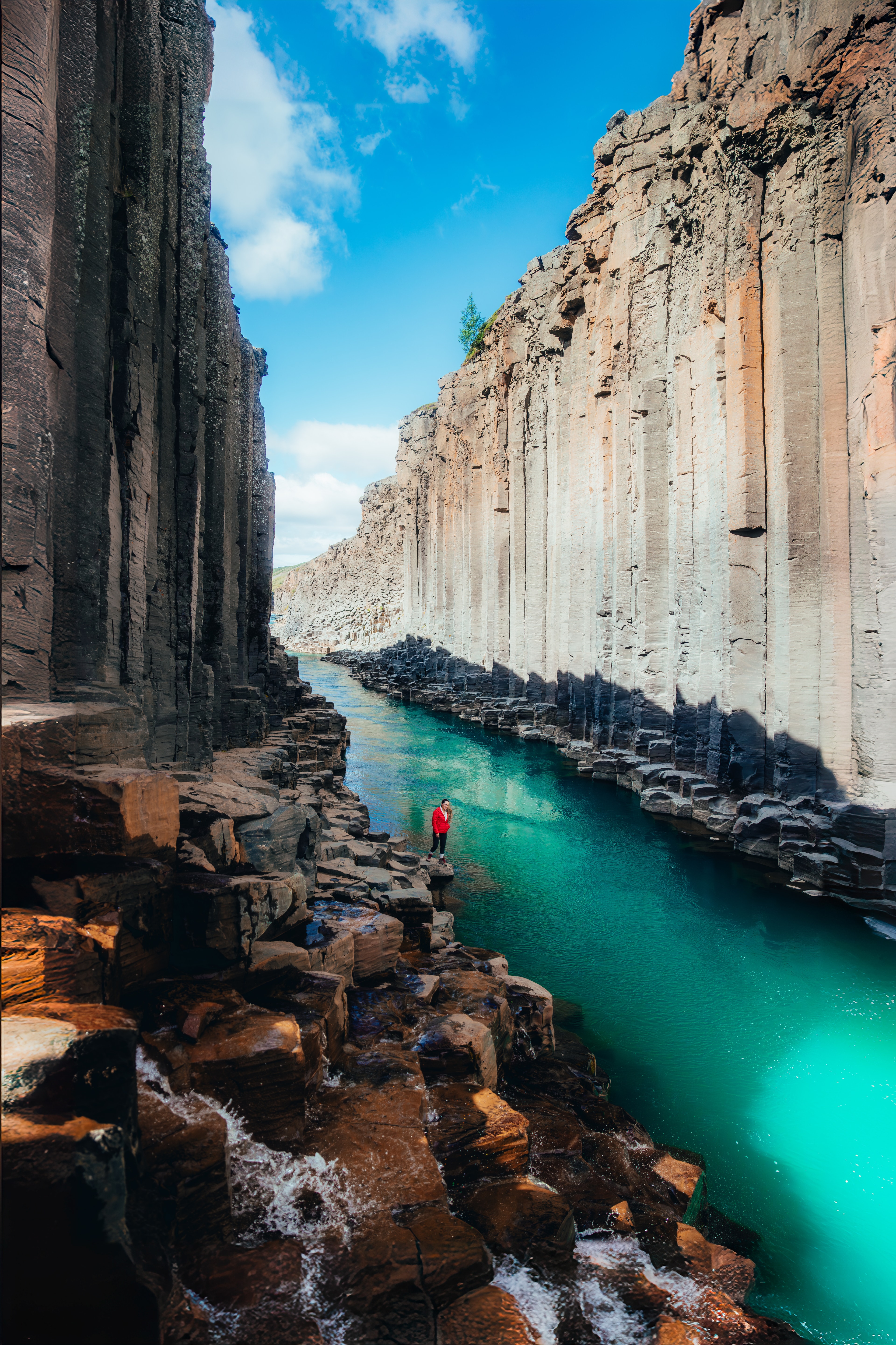 Studlagil canyon, a figure in red small against the towering basalt and turquoise river