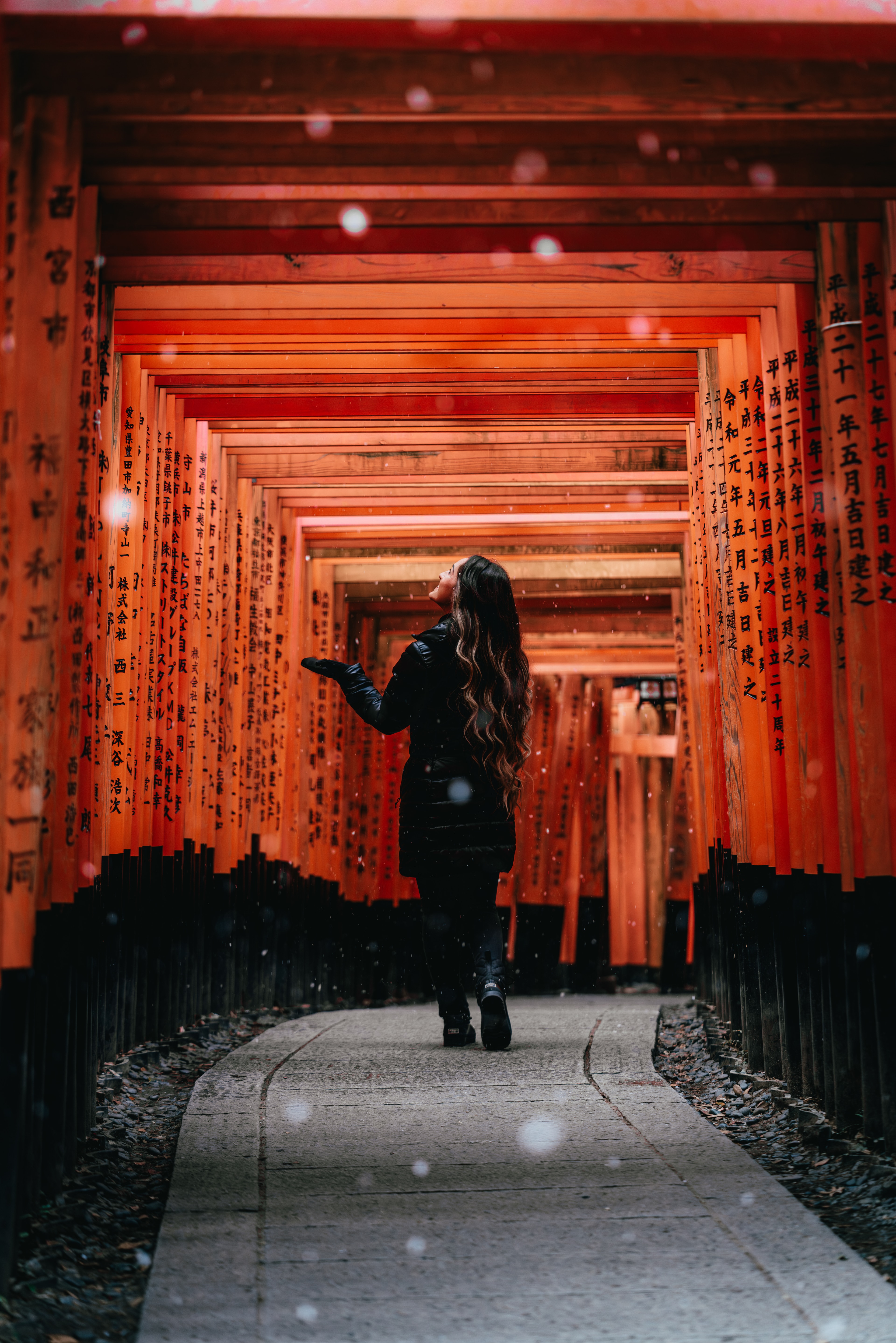 A figure beneath the vermilion torii gates of Fushimi Inari, snow in the air
