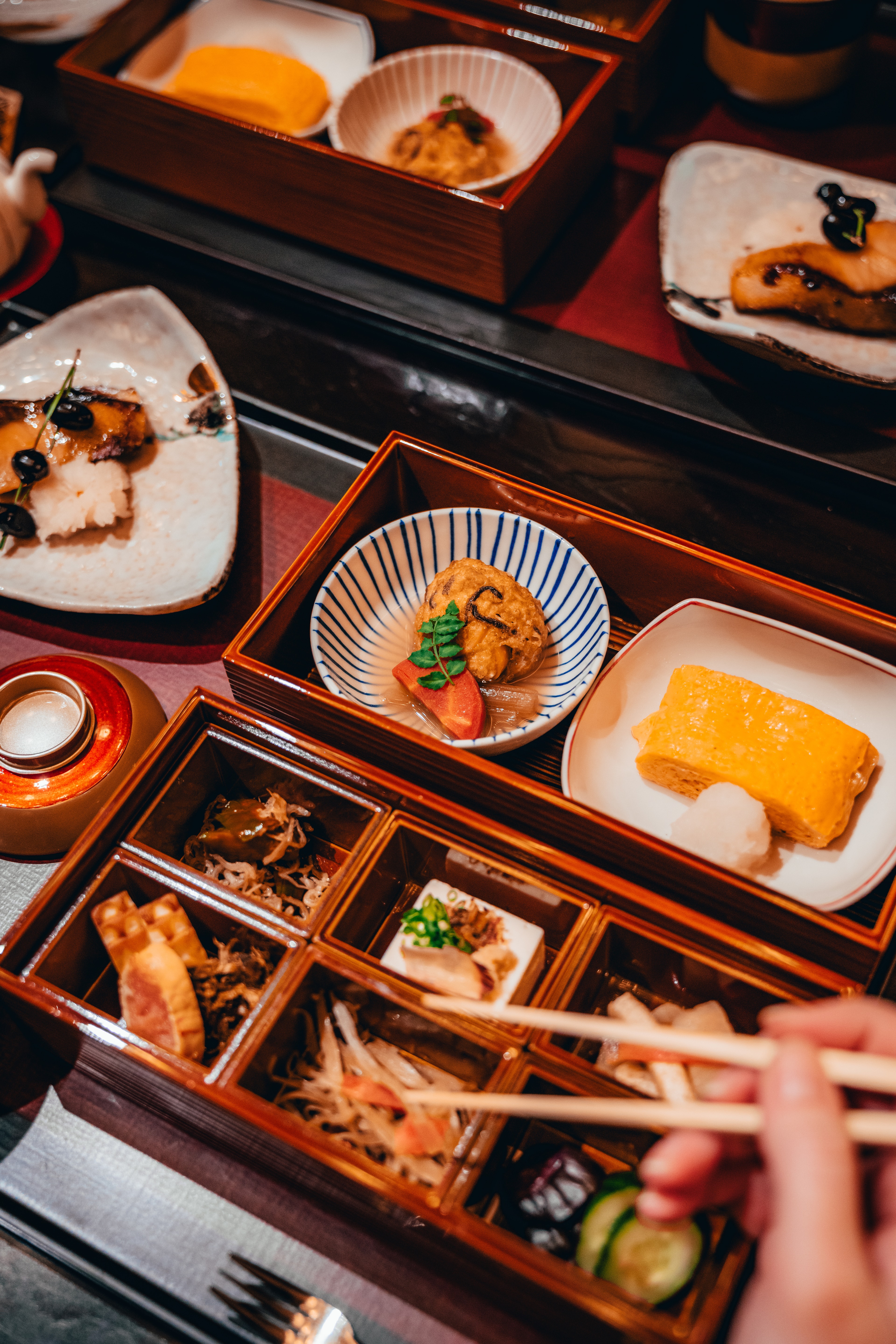 A kaiseki breakfast laid out in lacquer boxes, chopsticks lifting a bite
