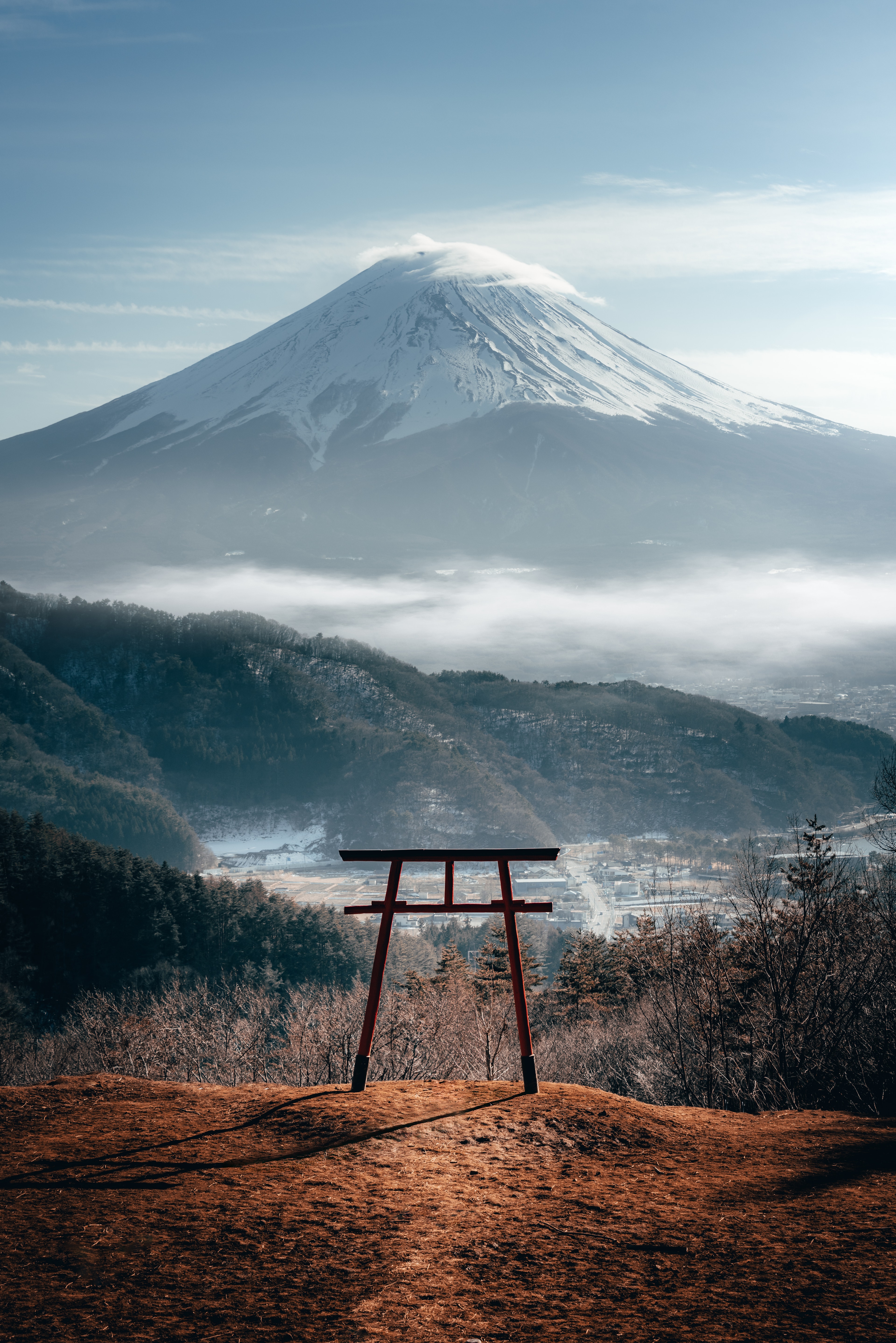 A red torii gate on a ridge with Mt Fuji floating above a sea of cloud