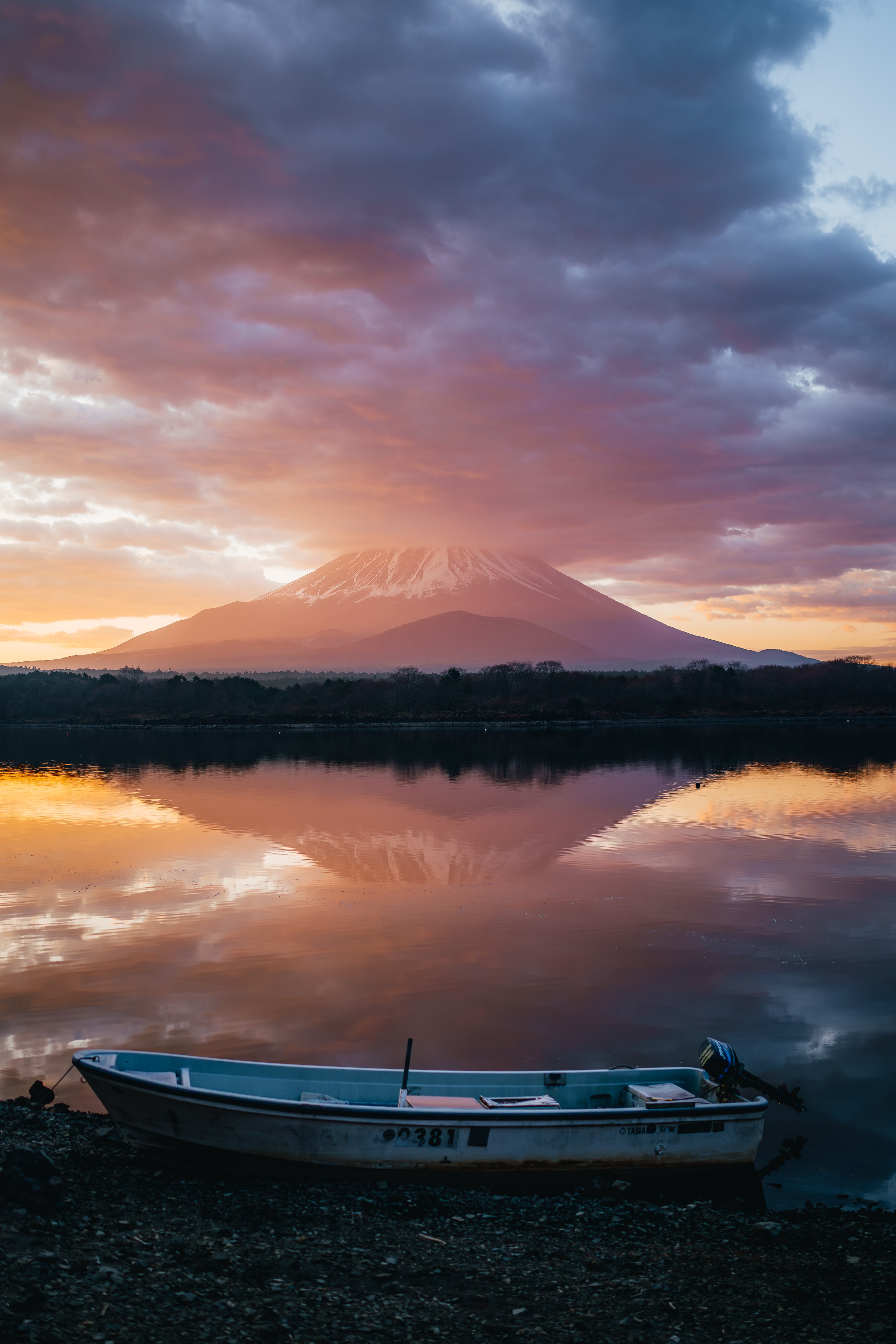 A wooden boat on a still lakeshore, Mt Fuji mirrored under a pink and orange sunset