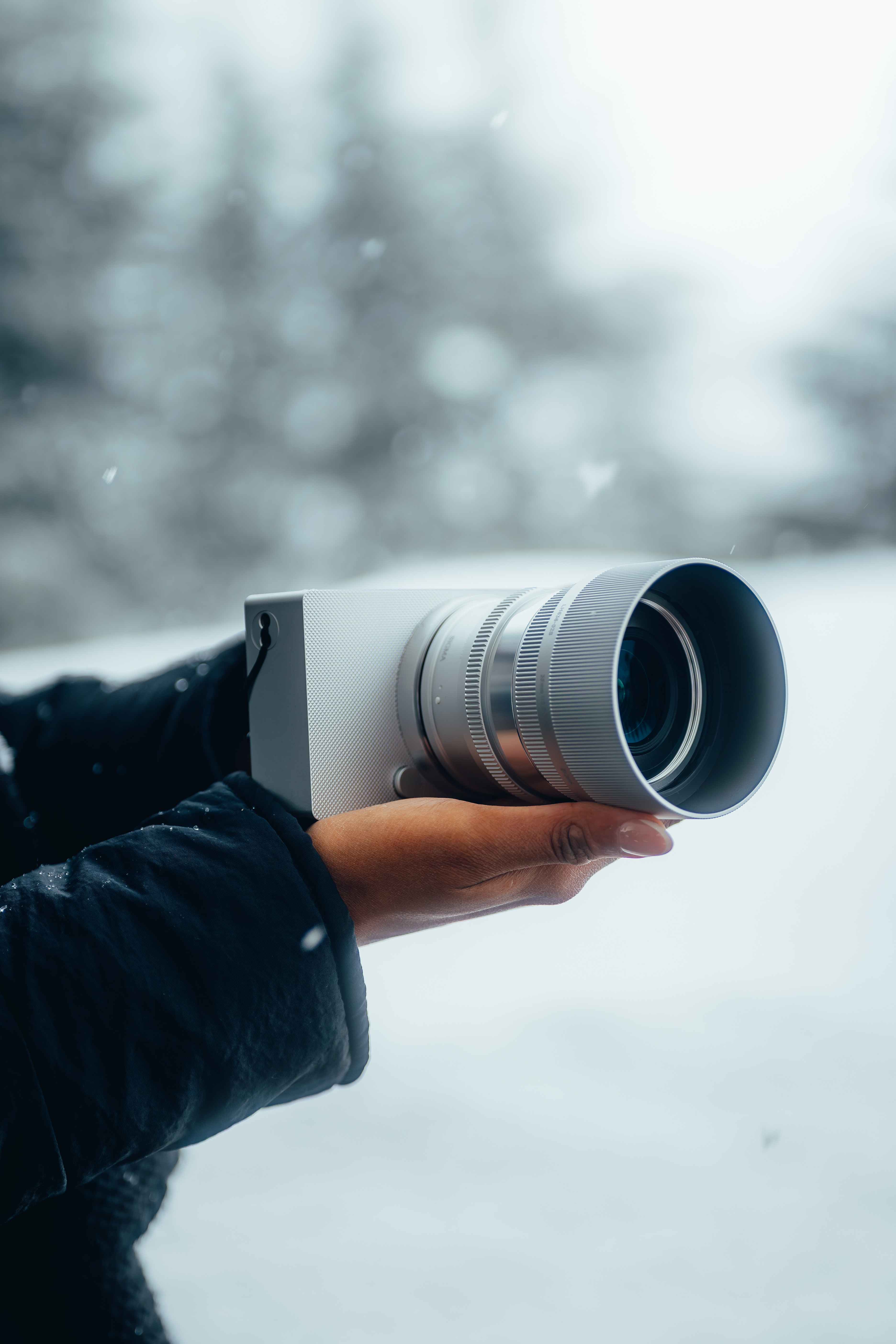 A hand holding the Sigma BF camera against a soft, snow-dusted backdrop