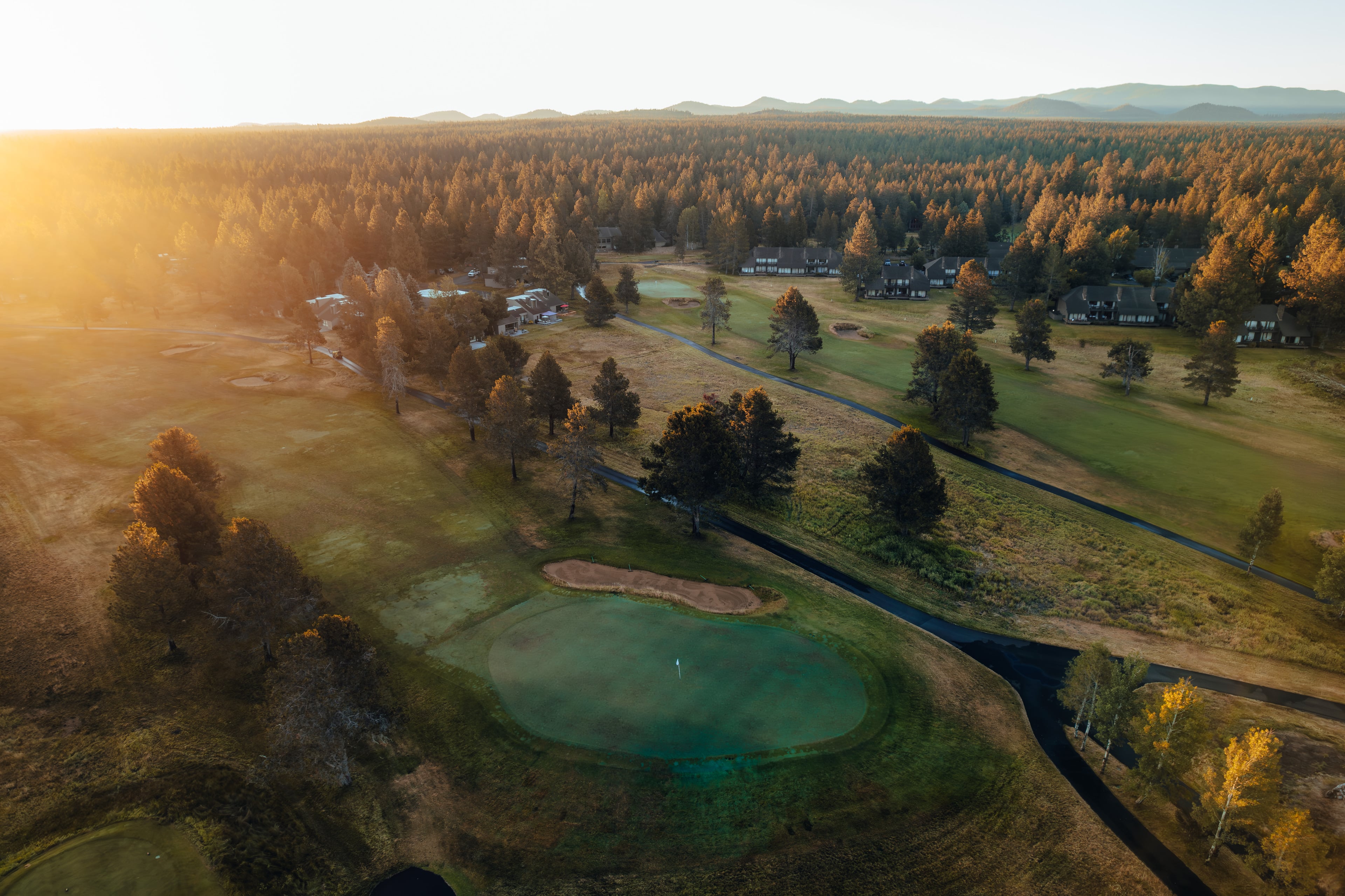 Sunrise aerial over the lodge pond, sun breaking through the pines